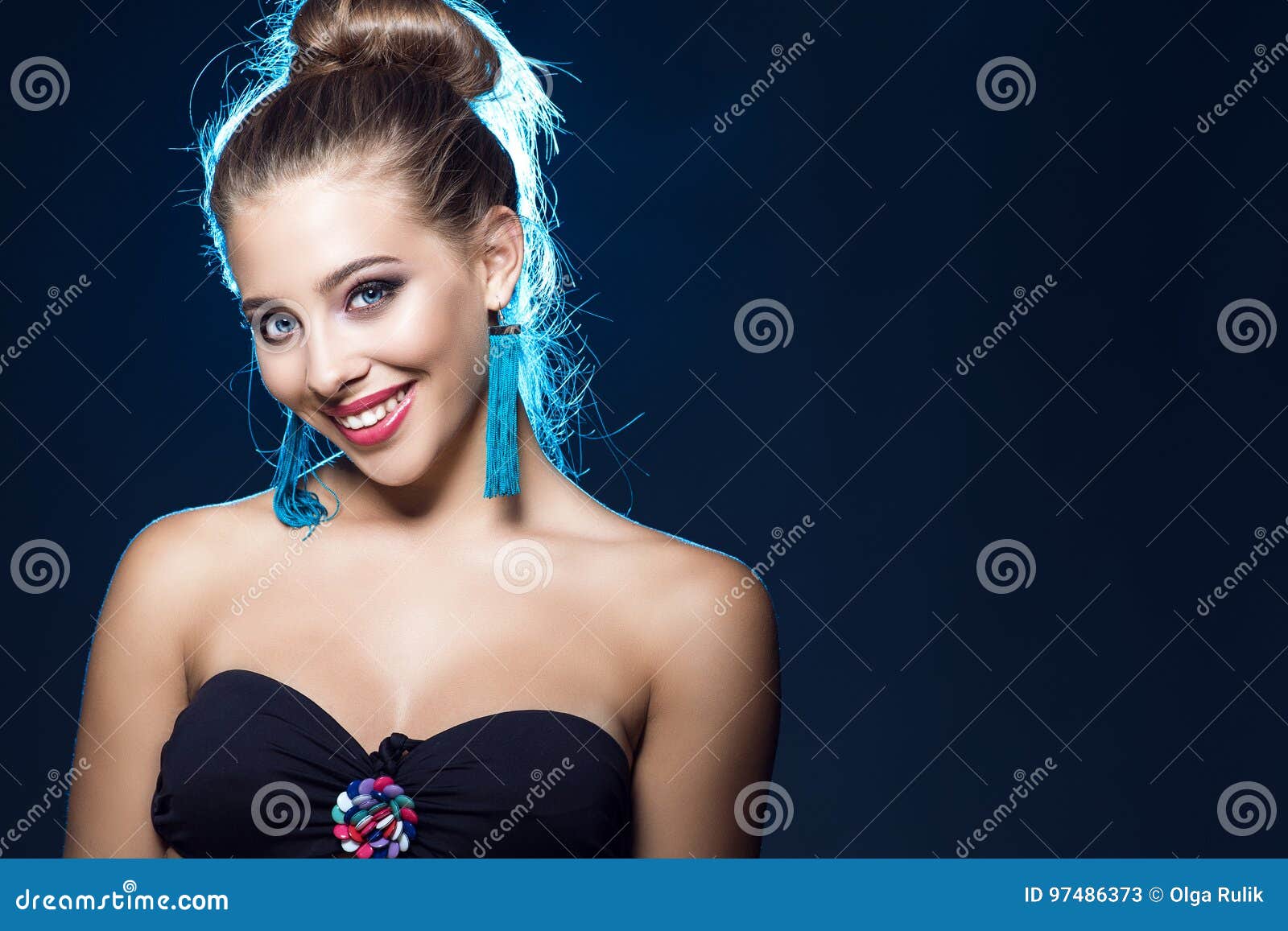 beautiful smiling blue-eyed young girl with perfect make up wearing black strapless bra and blue tassel earrings