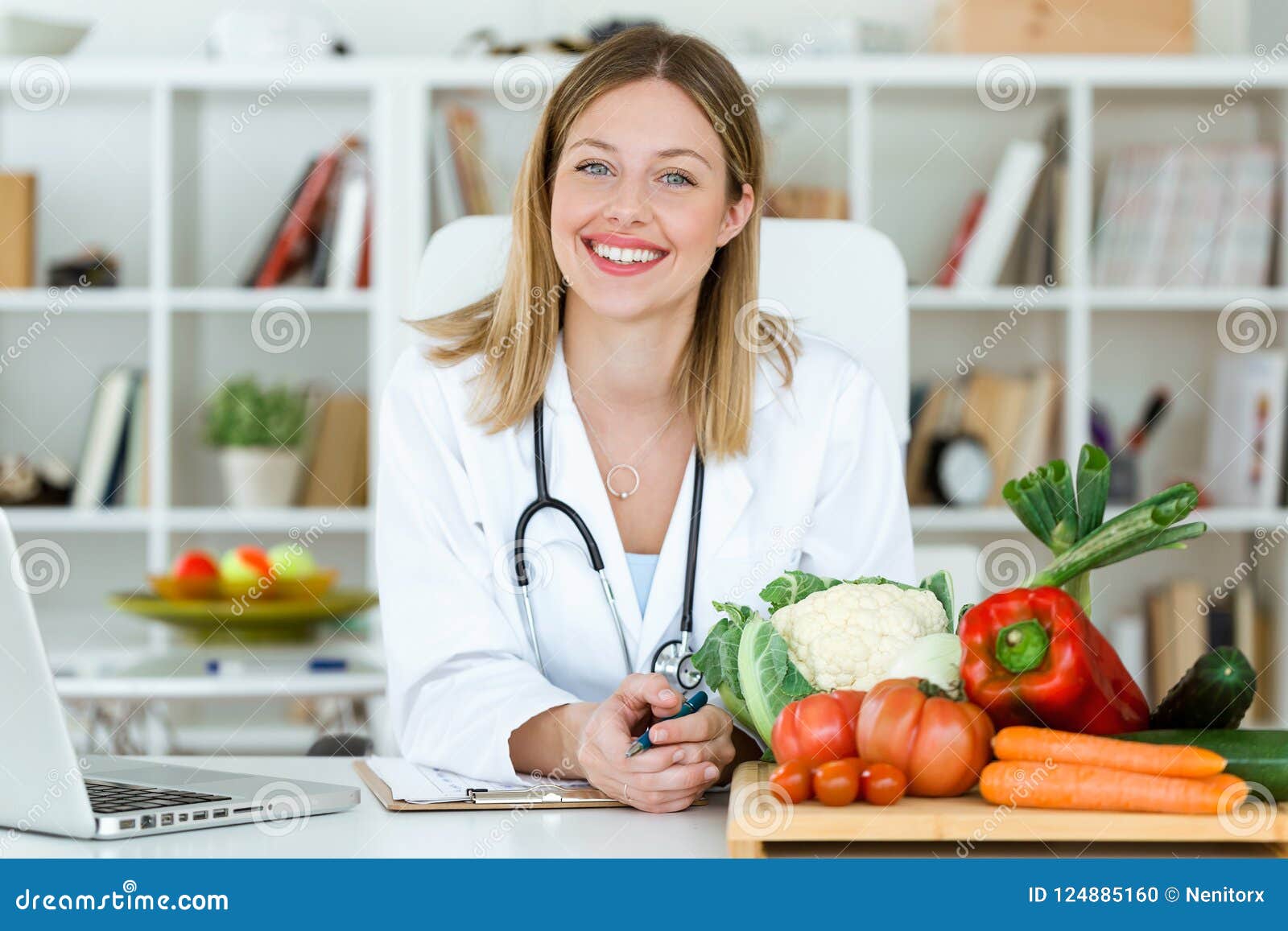 beautiful smiling nutritionist looking at camera and showing healthy vegetables in the consultation.