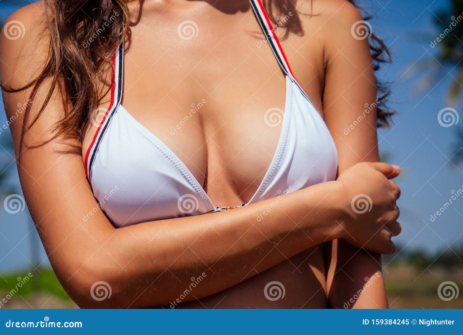 Foto de beautiful tanned female fitness big boobs model holding spf bottle  applying on the chest in a fashion stylish swimsuit on sea ocean beach blue  sky and palm trees background.summer vacation