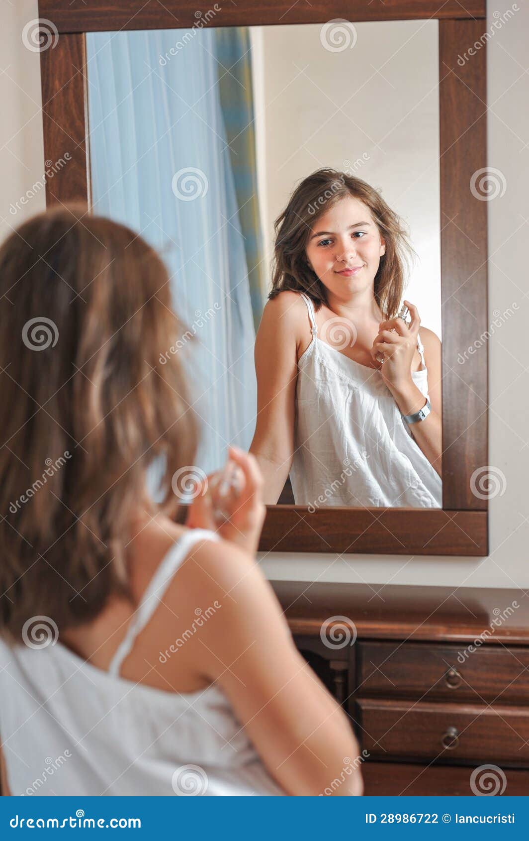 A Beautiful Teen Girl Studies Her Appearance As she Looks into the Mirror Stock Photo photo