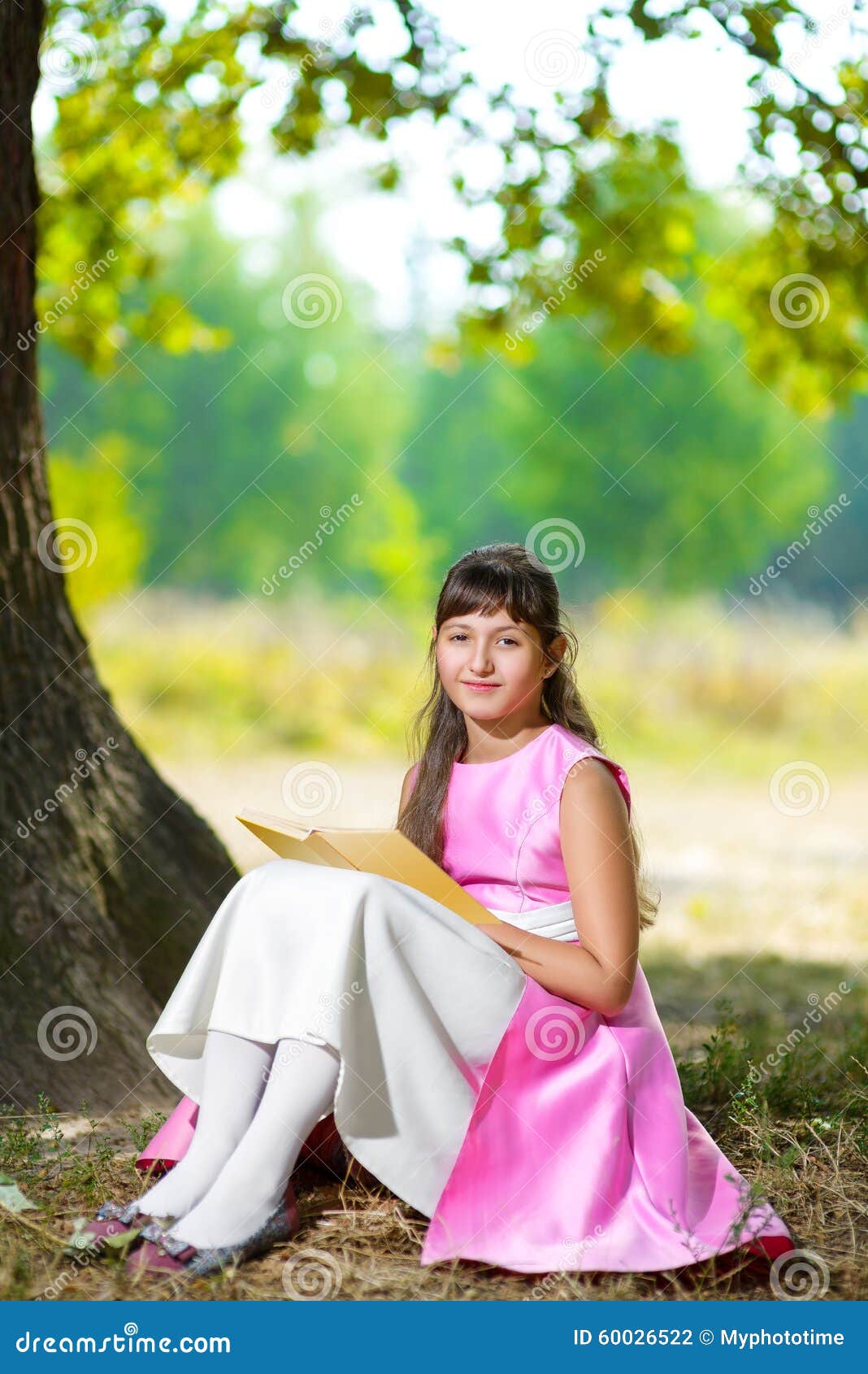 Beautiful teenage girl reads the book under huge. Beautiful teenage girl reads the book under the huge oak tree on sunny summer day.