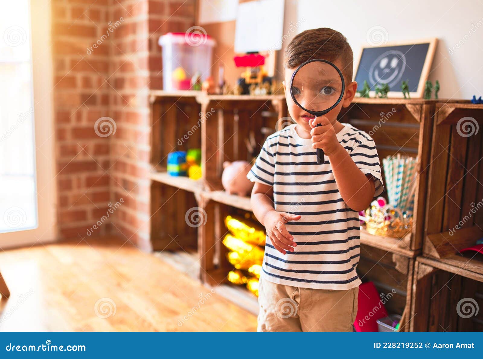 Beautiful Toddler Boy Using Magnifying Glass at Kindergarten Stock