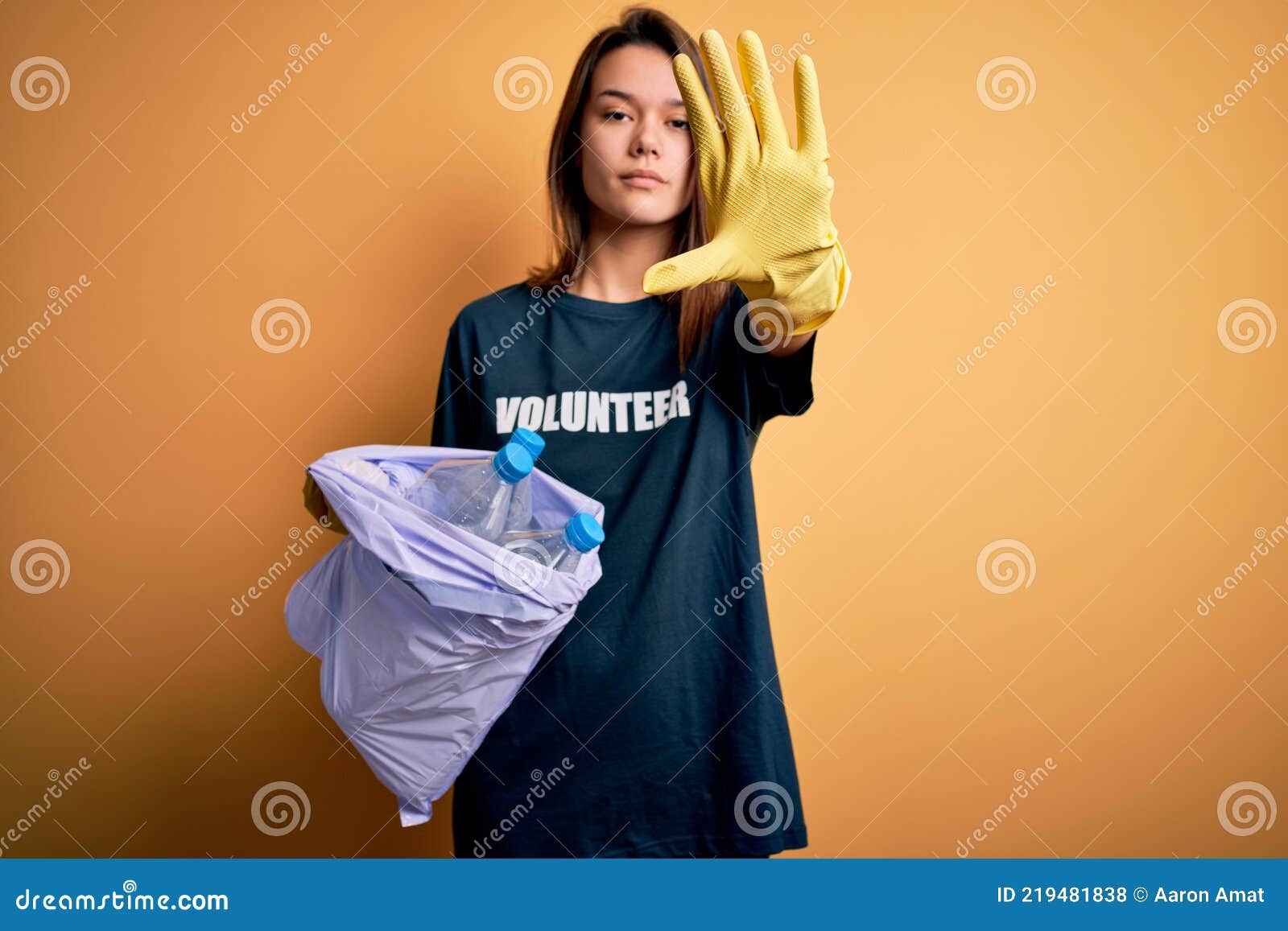 beautiful volunteer girl caring environment doing volunteering holding bag with rubish bottles with open hand doing stop sign with
