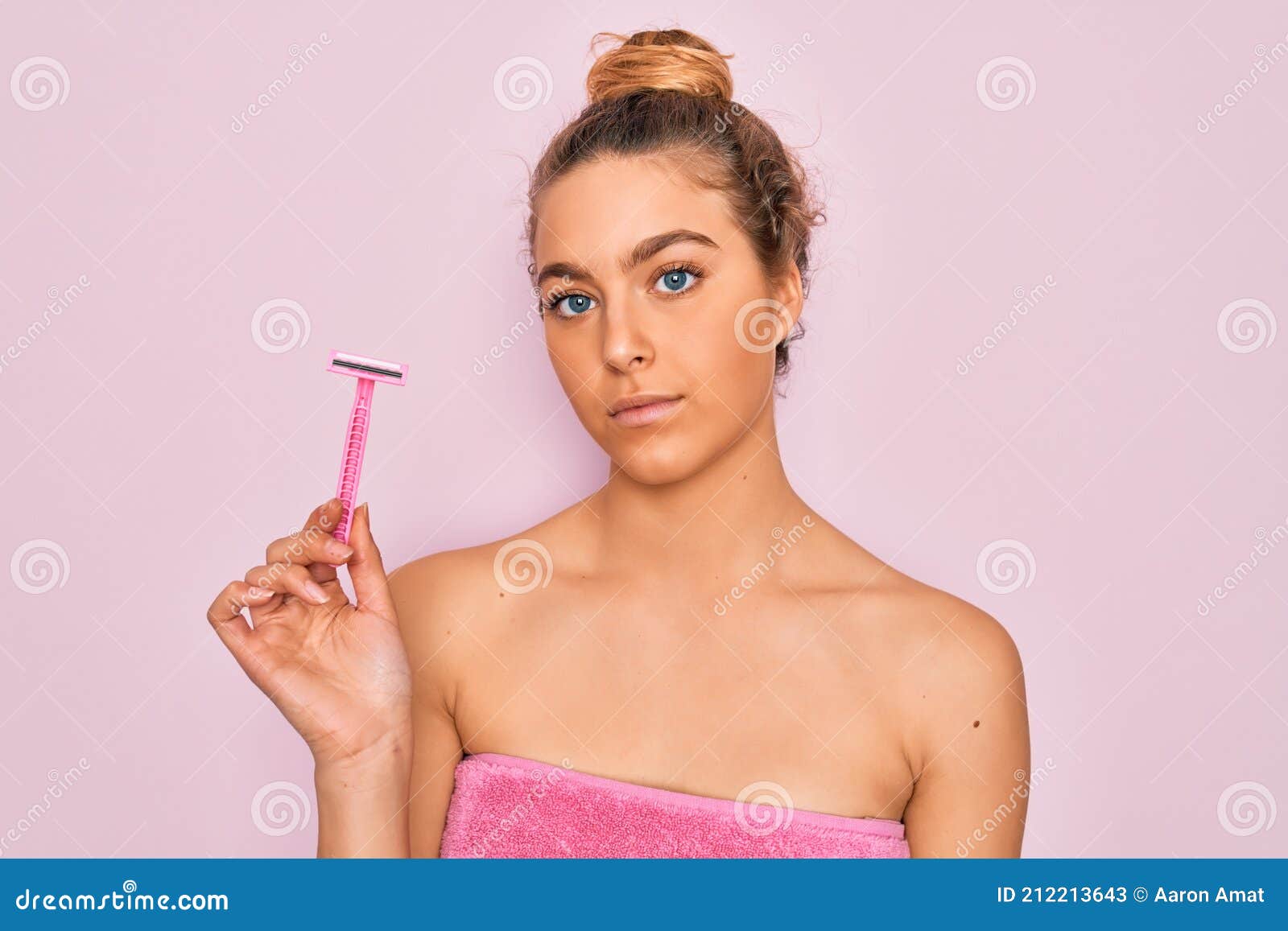 beautiful woman with blue eyes wearing towel shower after bath holding depilation razon with a confident expression on smart face