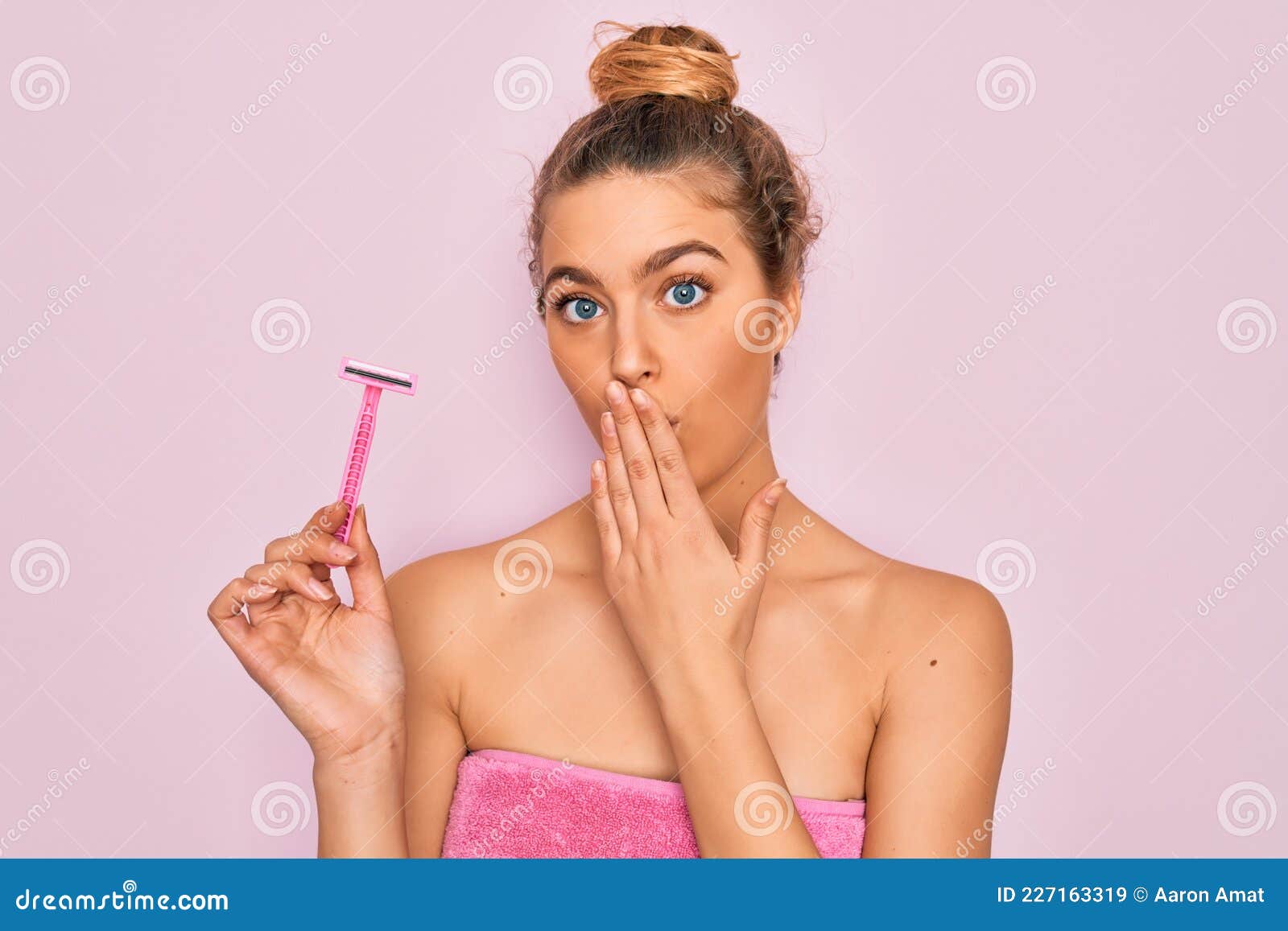 beautiful woman with blue eyes wearing towel shower after bath holding depilation razon cover mouth with hand shocked with shame
