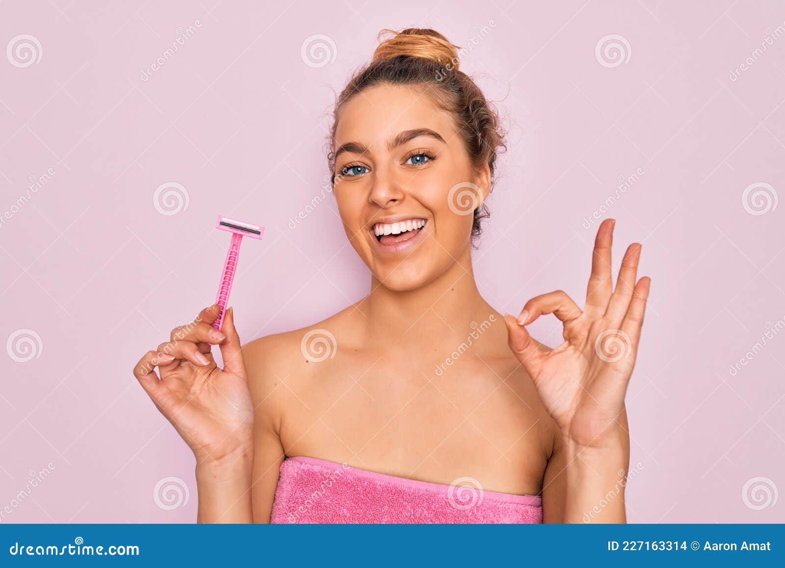 beautiful woman with blue eyes wearing towel shower after bath holding depilation razon doing ok sign with fingers, excellent