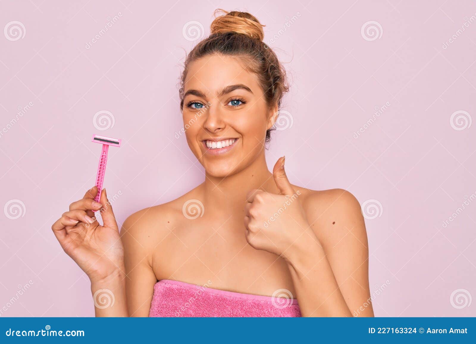 beautiful woman with blue eyes wearing towel shower after bath holding depilation razon happy with big smile doing ok sign, thumb