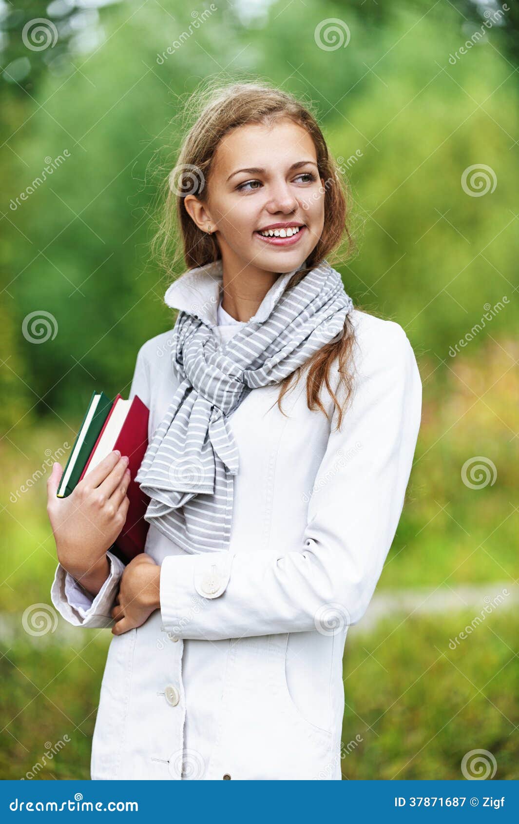 Young happy beautiful woman with books, against background of autumn park.