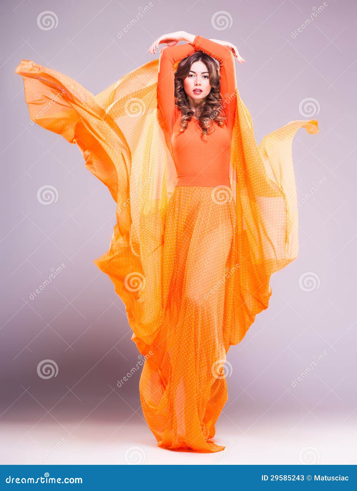 beautiful woman in long orange dress posing dramatic in the studio