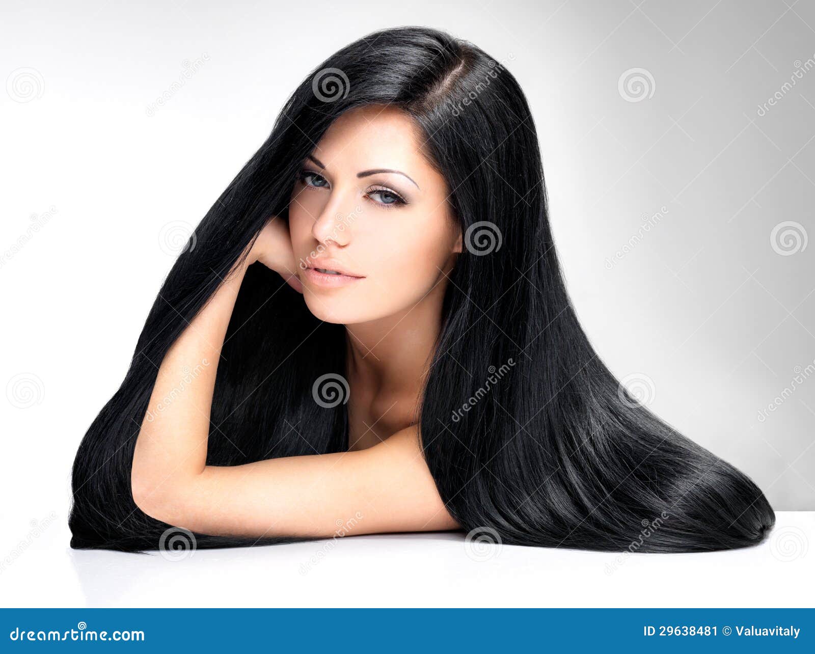 Beautiful brunette young woman has long dark hair poses indoor against  blue studio background being successful businesswoman has natural look  enjoys leisure or day off stands delighted  a Royalty Free Stock