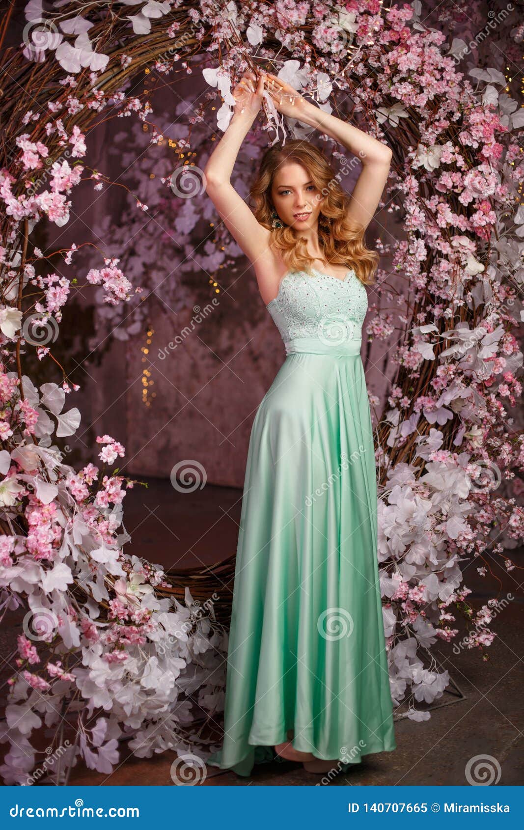 Beautiful Woman Model in a Mint-colored Dress on a Flowered Spring Background. Beauty Girl with