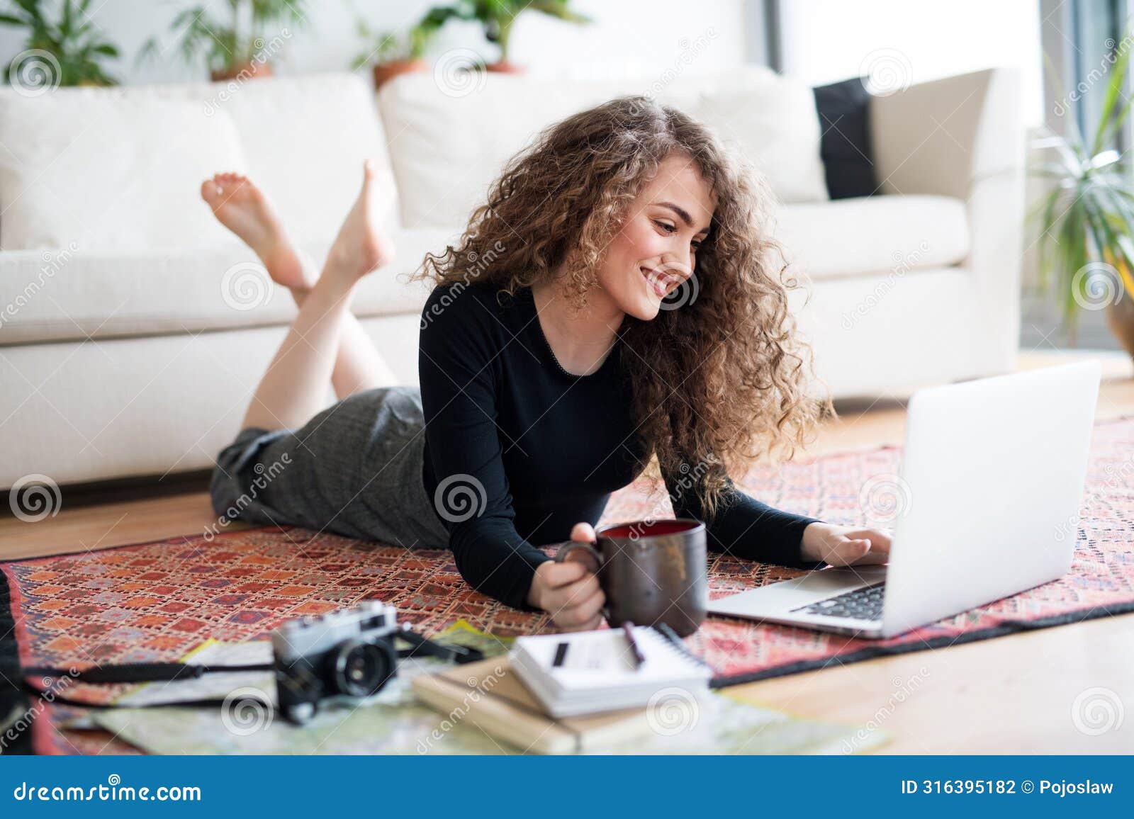 beautiful woman planning summer vacation abroad, going on trip alone. lying on floor, working on itinerary on laptop.