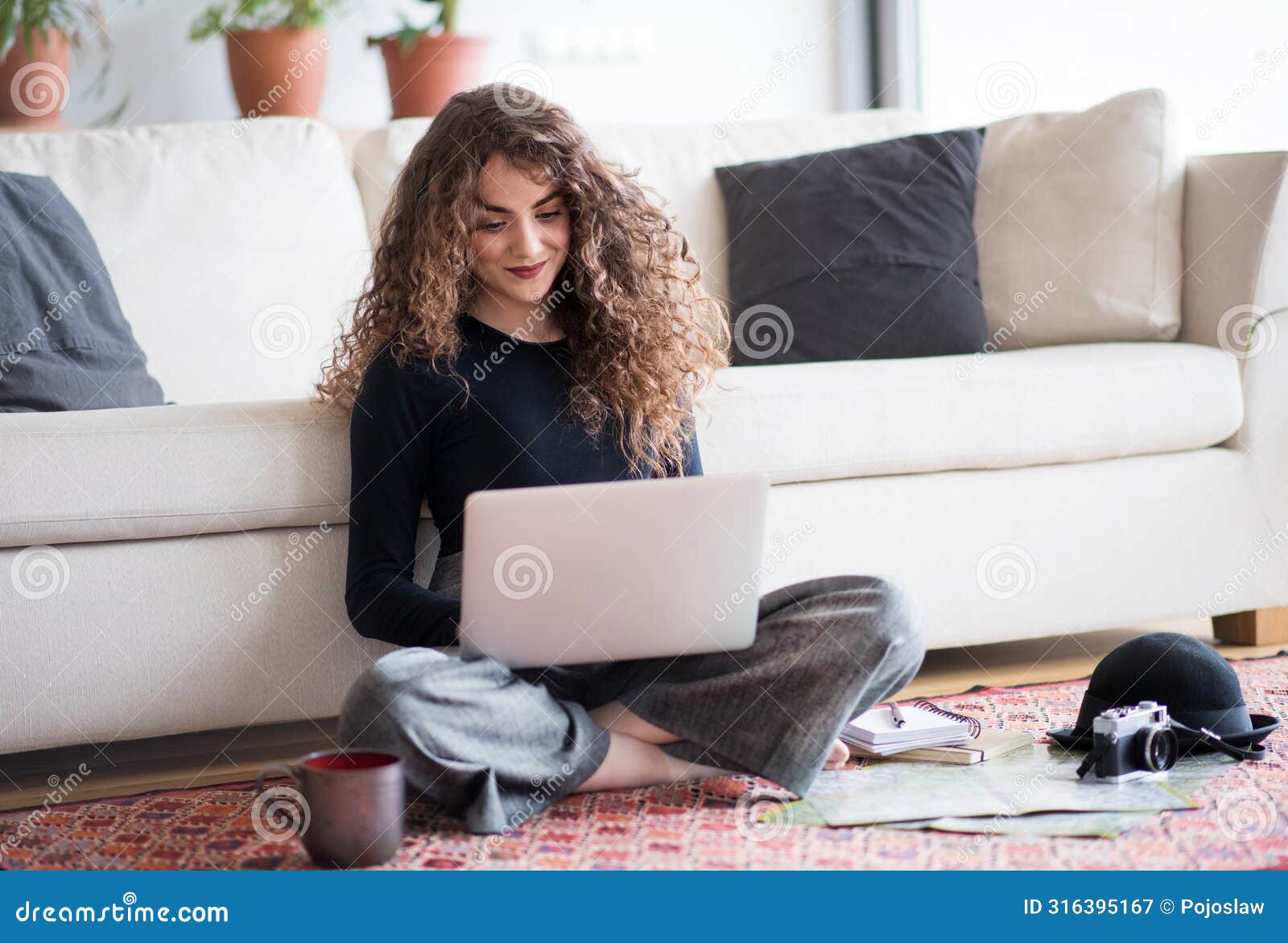 beautiful woman planning summer vacation abroad, going on trip alone. sitting on floor, working on itinerary on laptop.