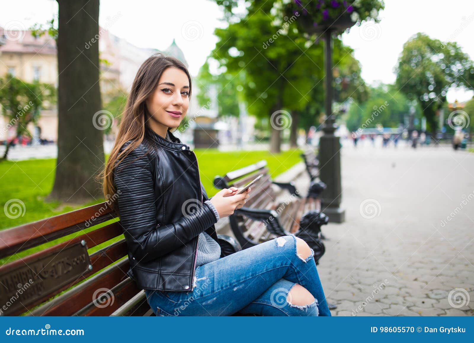 Young Woman Sitting On Bench On The Street And Using Her 