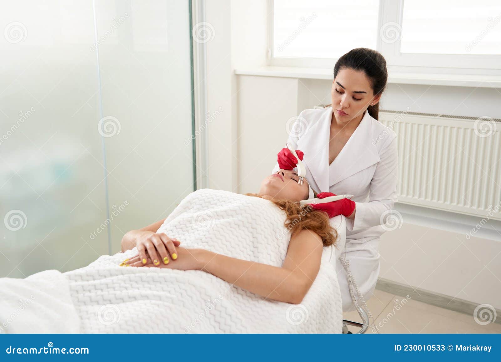 Beautiful Woman In Spa Clinic Receiving Stimulating Electric Facial Treatment From Therapist