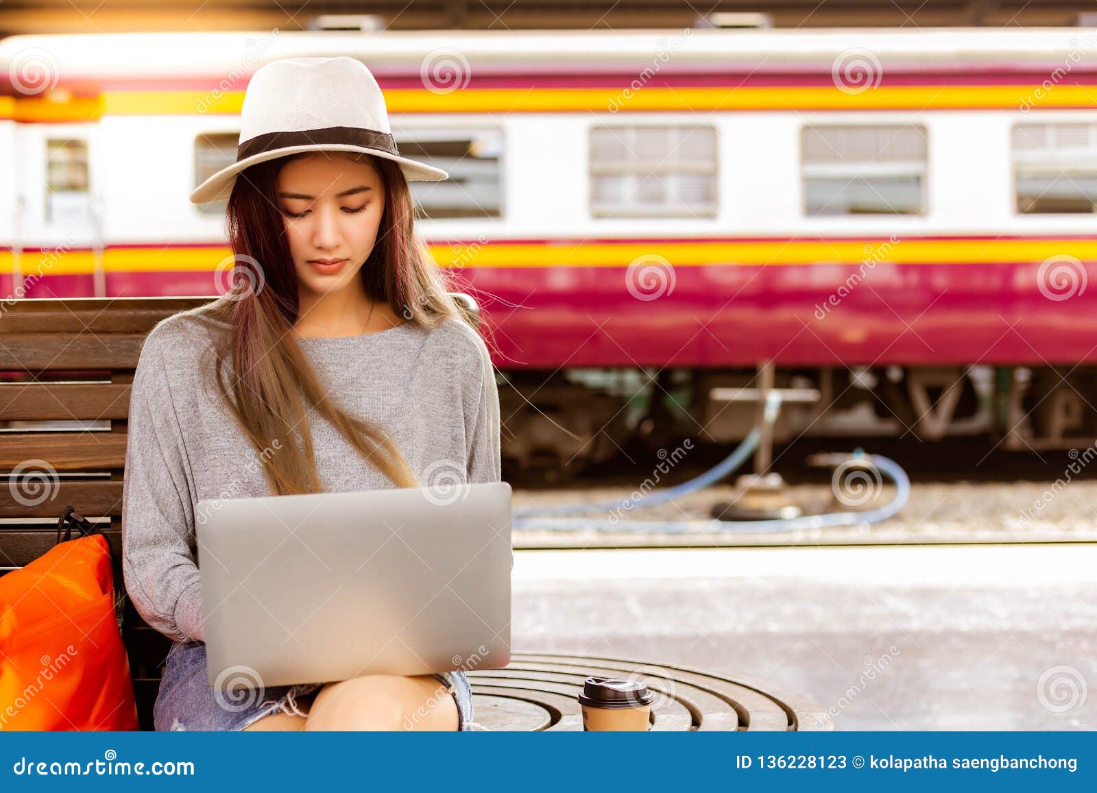 beautiful woman is using laptop at train station before charming beautiful asian woman travel to destination. she is a blogger and