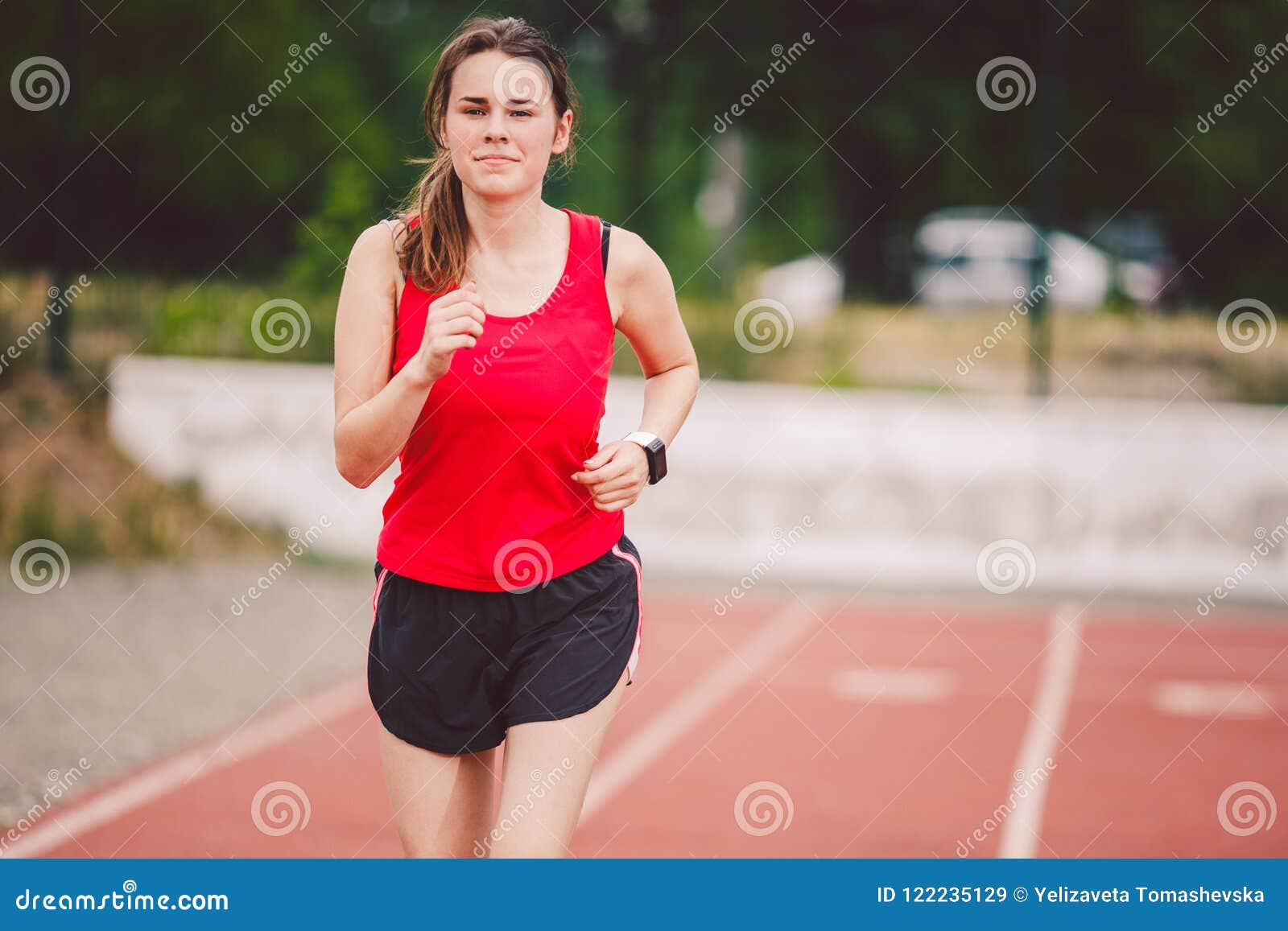 Theme is sport and health. Beautiful young caucasian woman with big breasts  athlete runner stands resting on running stadium, running track with bottle  in hands drinking water in short shorts Stock Photo