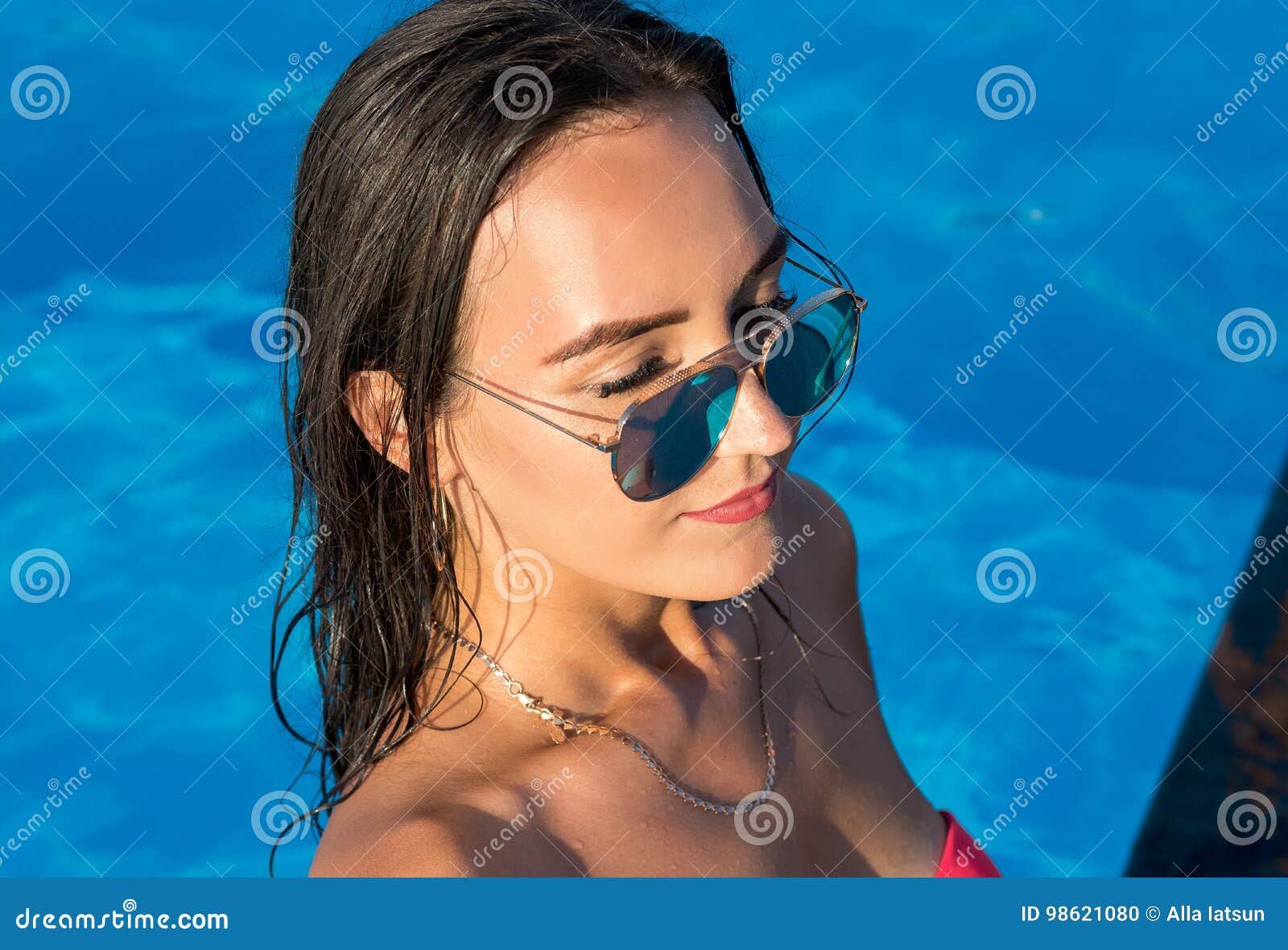 Beautiful young brunette woman with long wet hair in a pool in the summer.