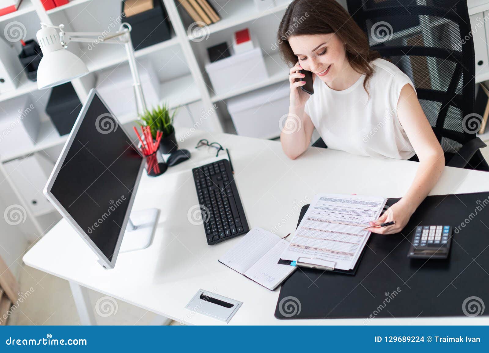 A Young Girl Sitting In The Office At The Computer Desk Talking