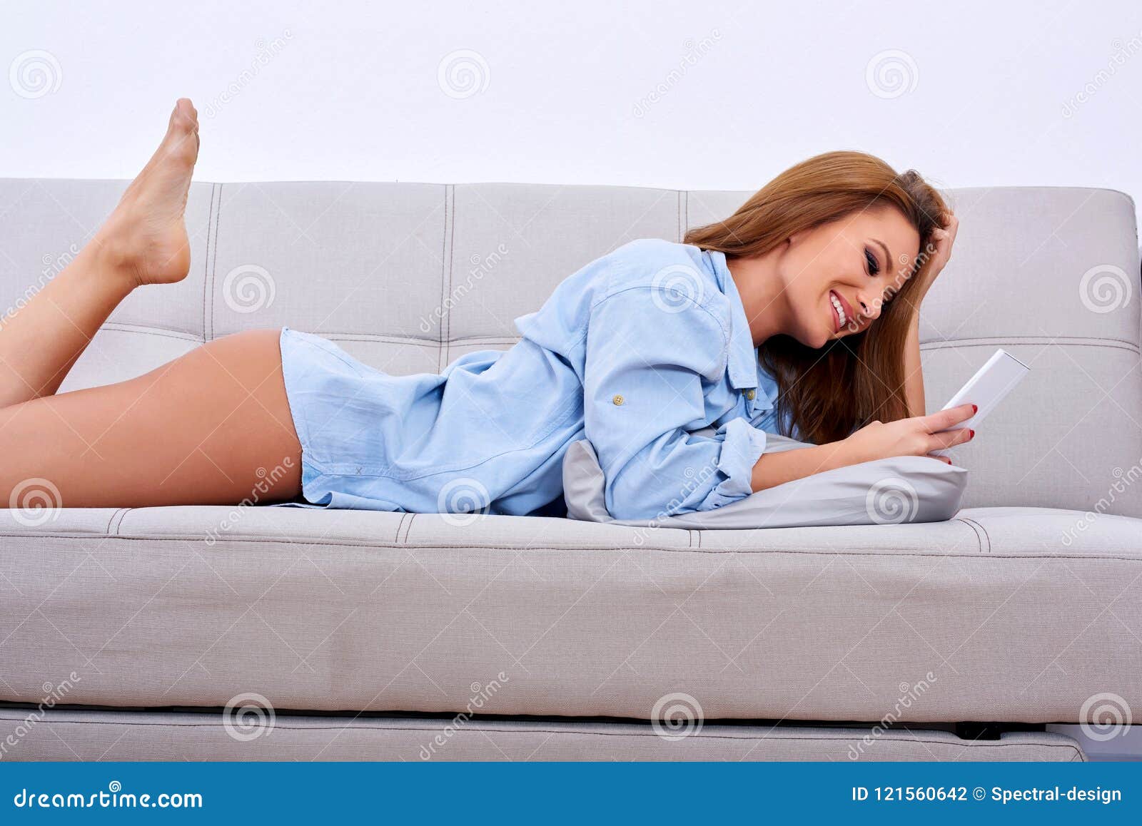 A Smiling Woman Laying on a Sofa and Using Her Smartphone Photo - Image of phone, nude: 121560642