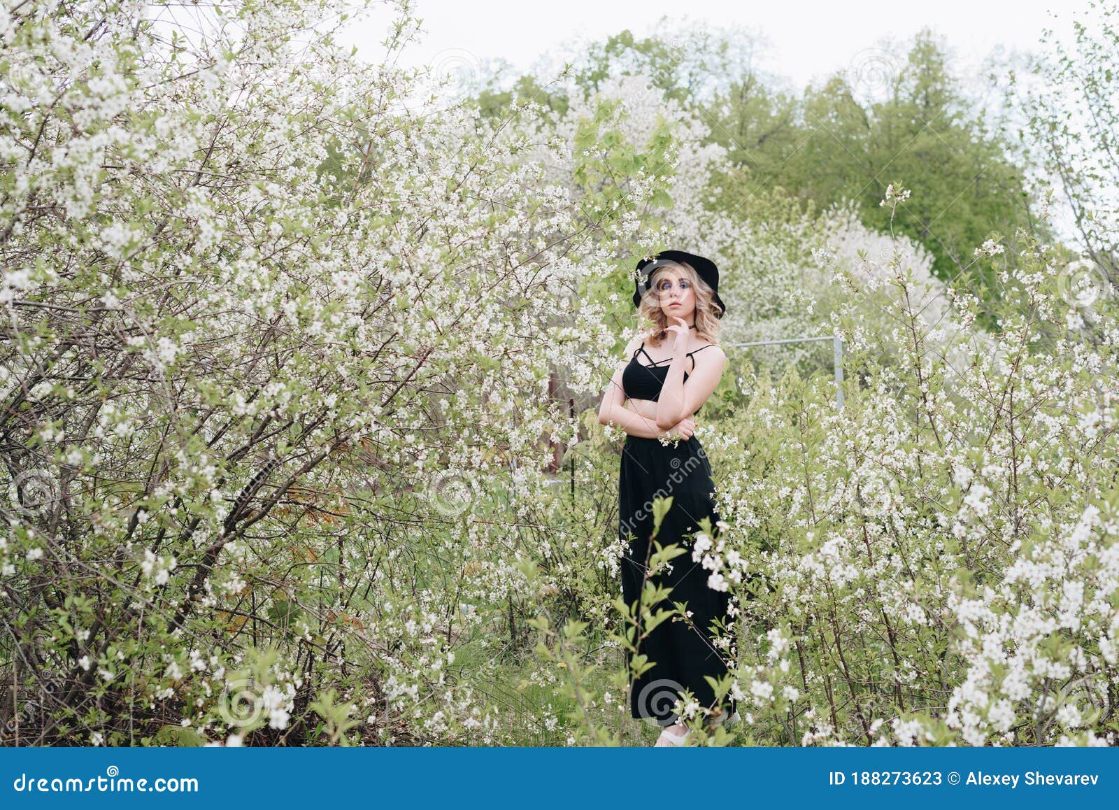 A Beautiful Young Woman in Black Clothes and a Hat in a Blooming Garden ...