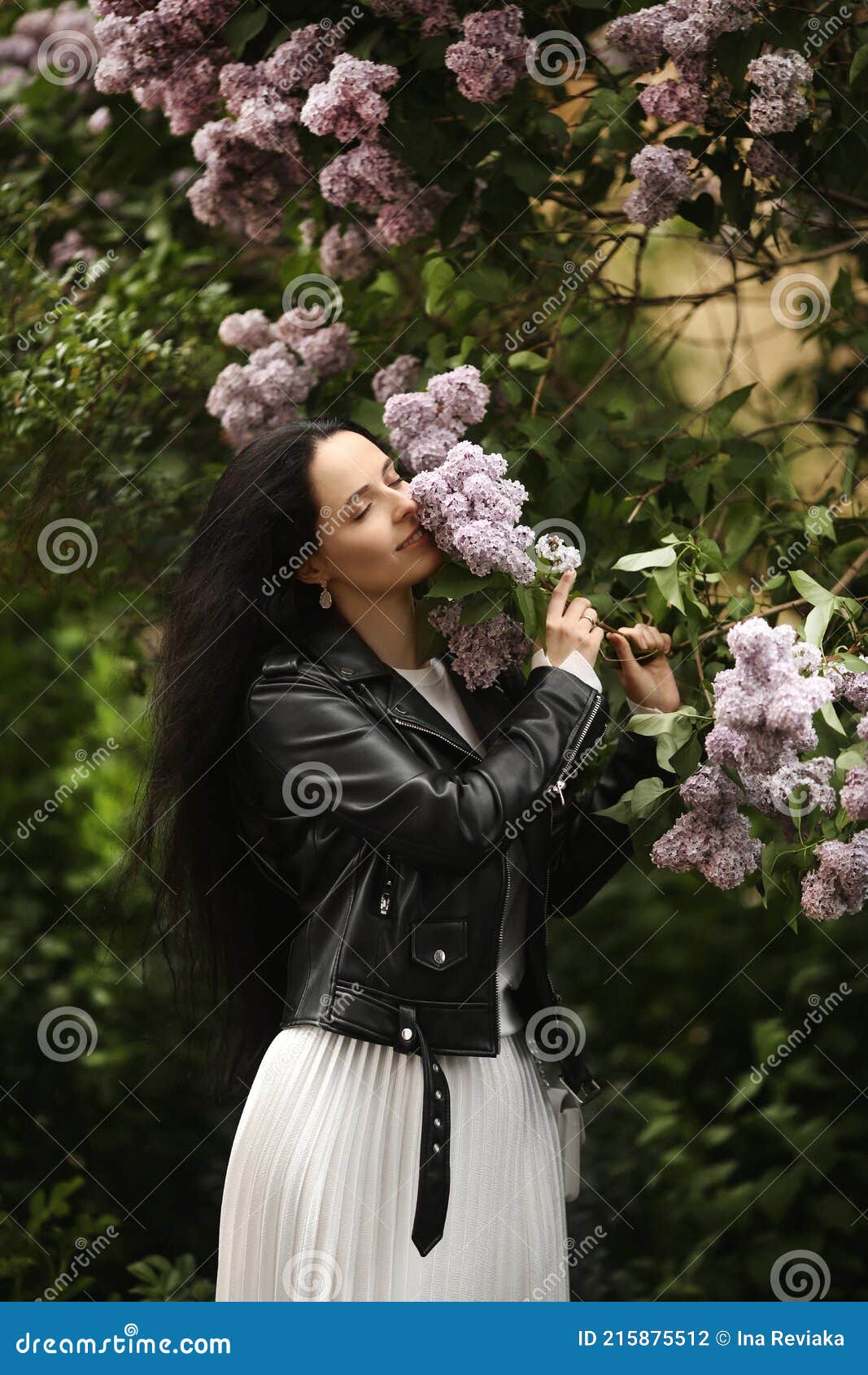 beautiful young woman in leather jacket enjoying the smell of the bloomy lilac tree in springtime