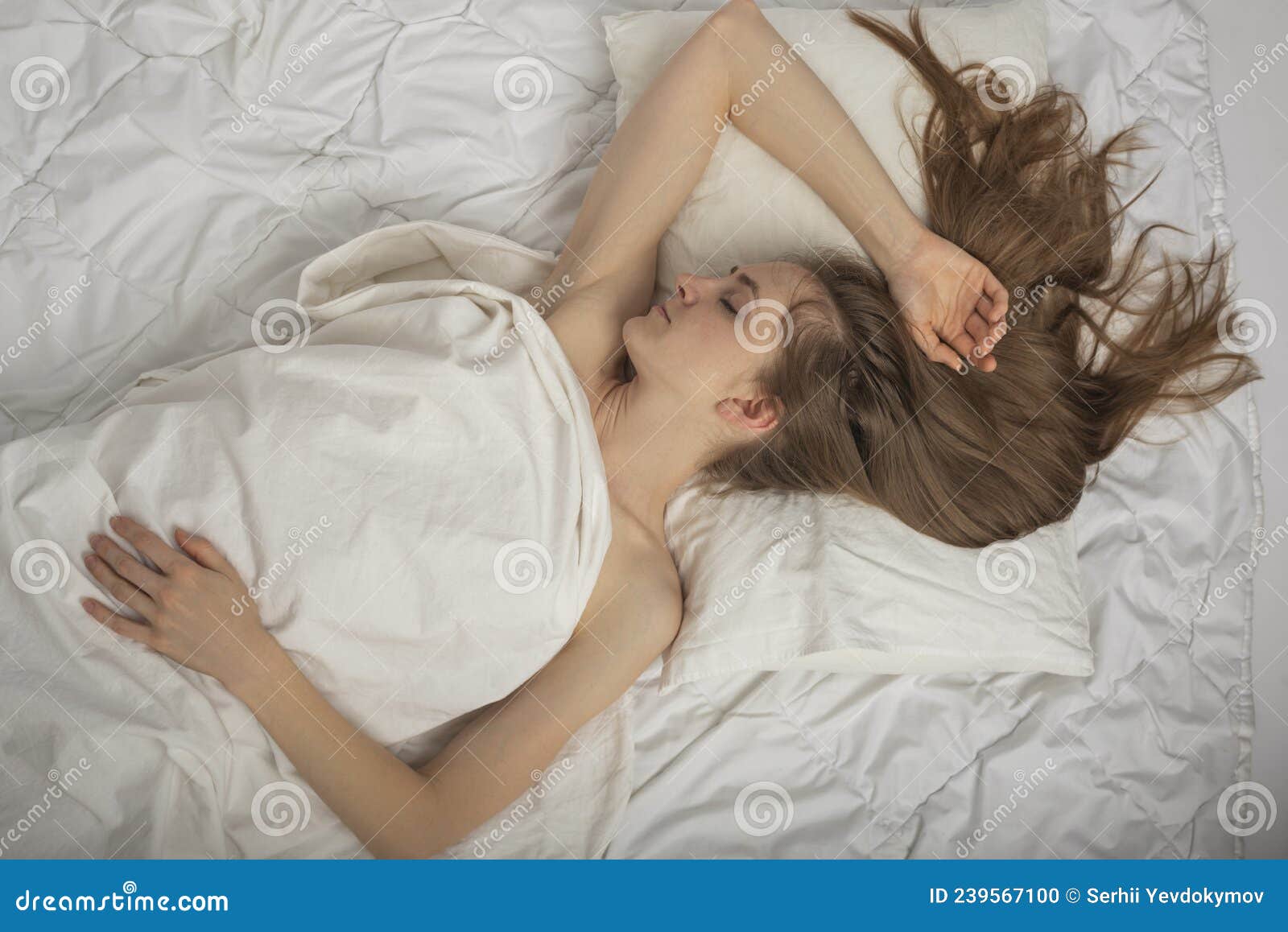 beautiful young woman with long hair sleeps soundly on expensive bed linen. portrait of sleeping girl top view