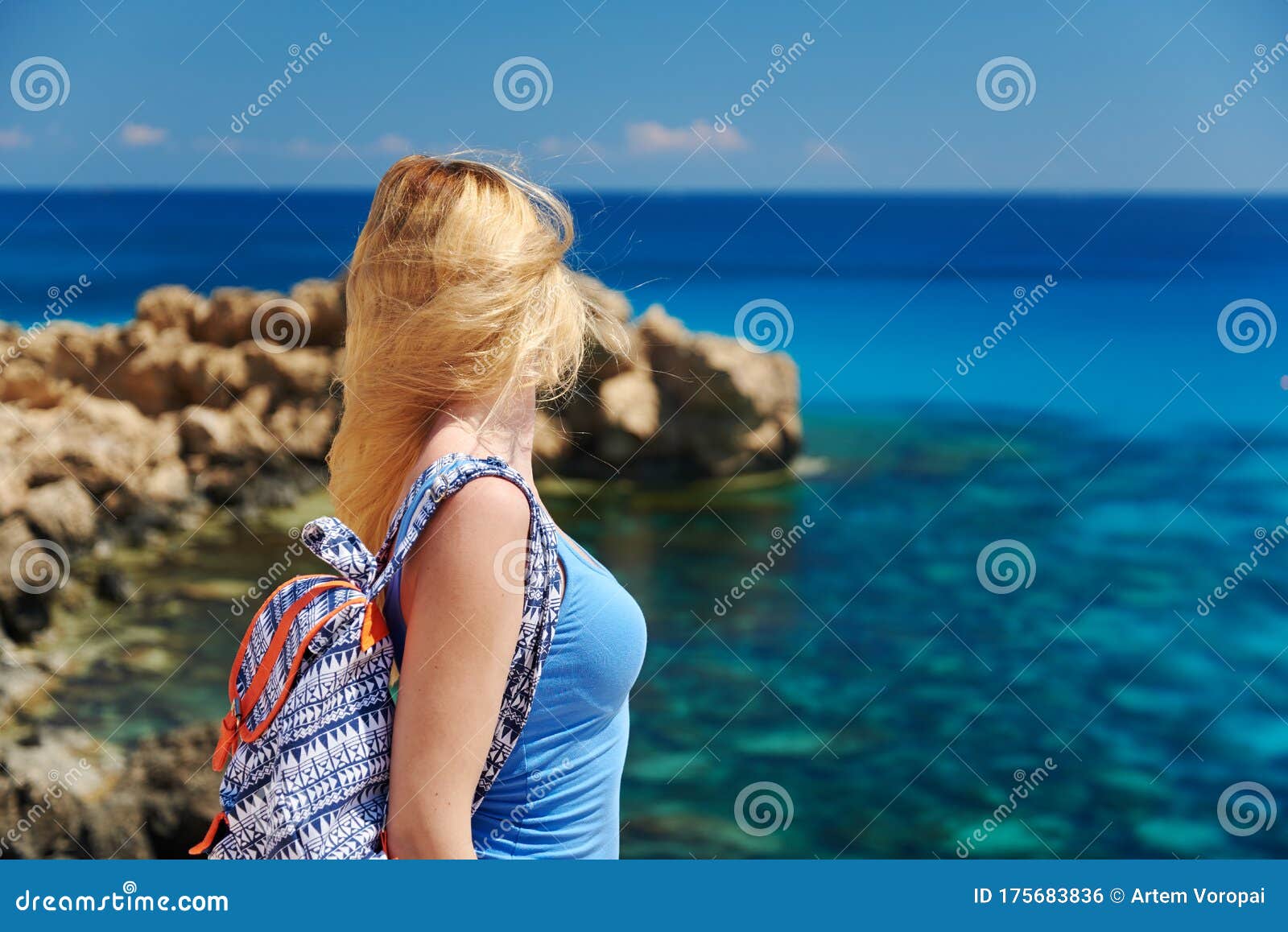 beautiful young woman is looking to the sea being on the picturesque cliffy coast.