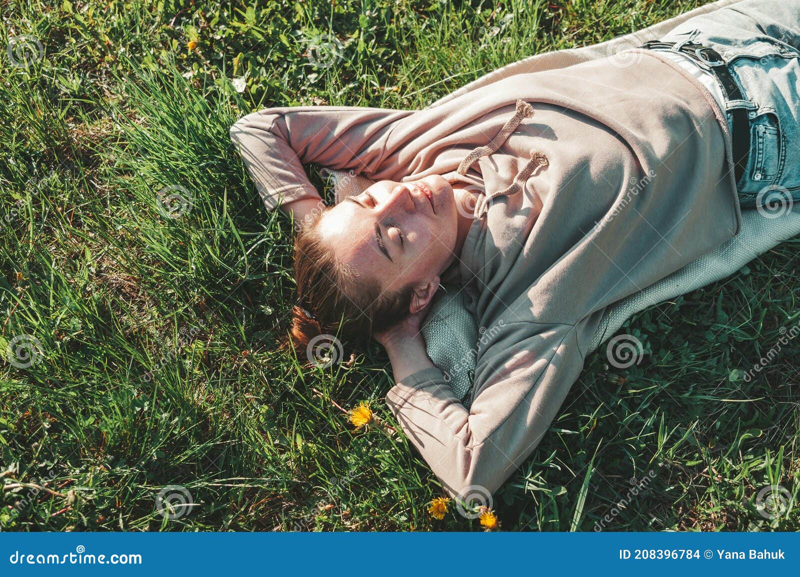 beautiful young woman lying on a field, green grass and dandelion flowers. outdoors enjoy nature. healthy smiling girl lying in