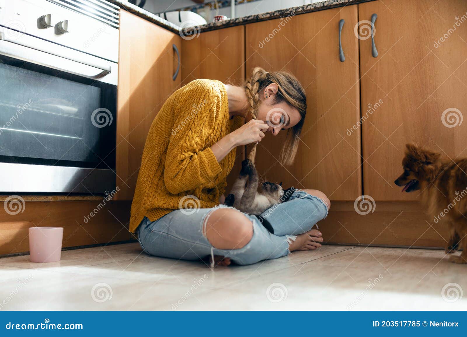 beautiful young woman playing with her cute lovely animals sitting on the floor in the kitchen at home