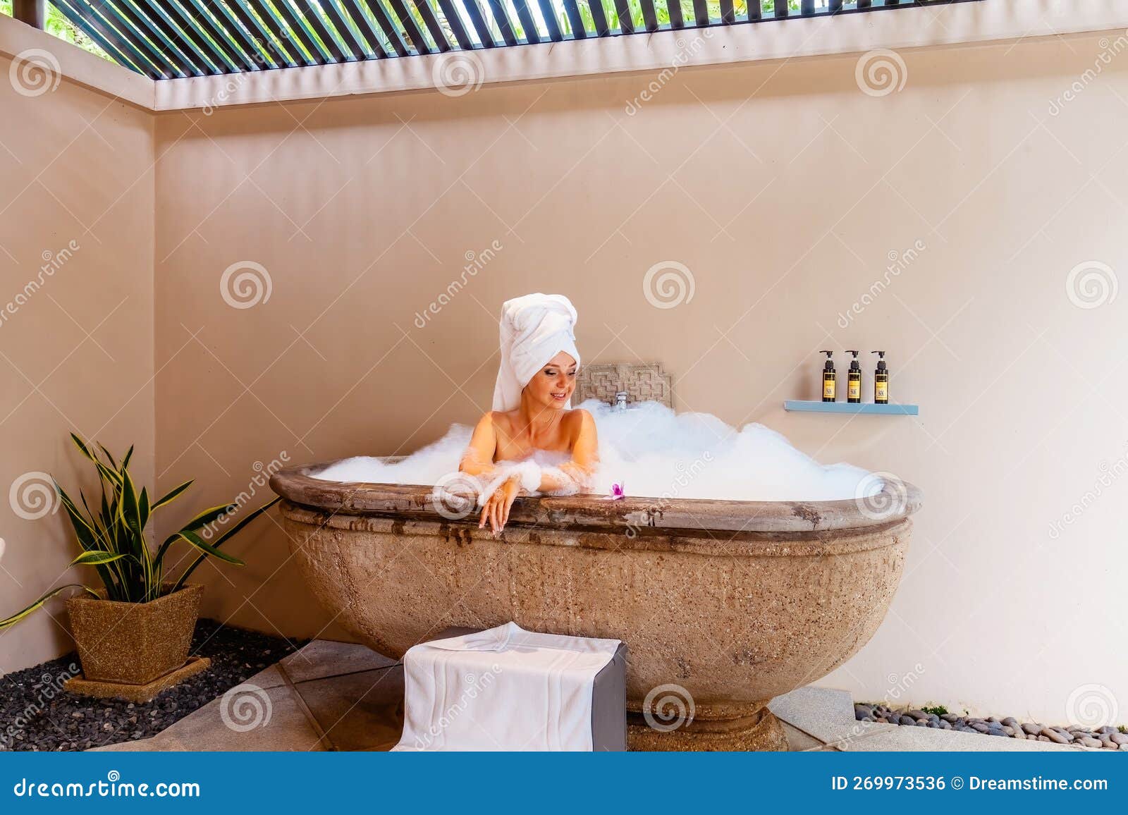 Beautiful Young Woman Relaxes In A Foam Filled Tub With Exotic Flowers 