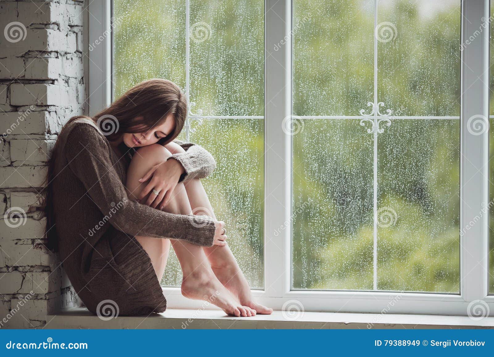 beautiful young woman sitting alone close to window with rain drops. and sad girl. concept of loneliness