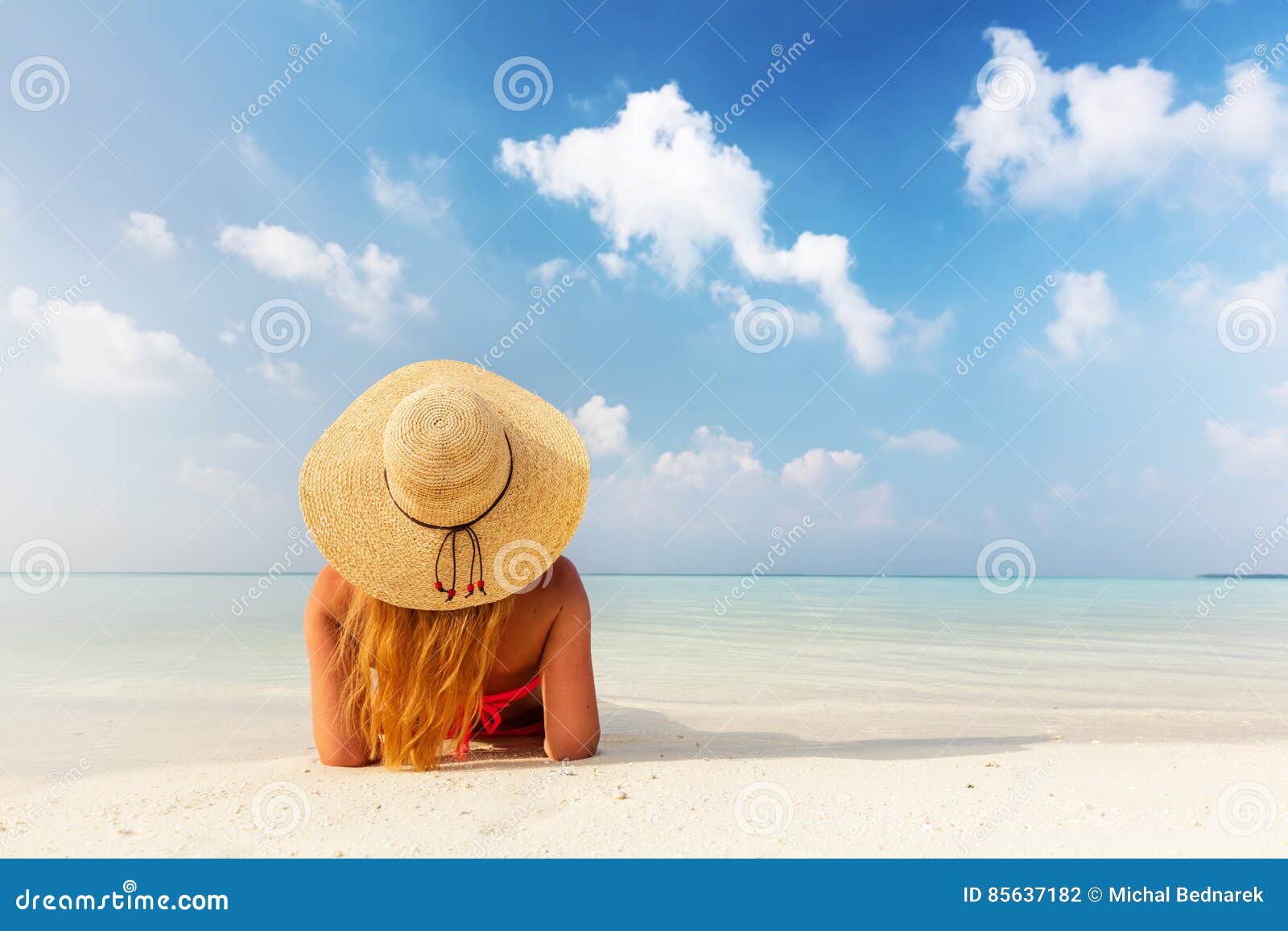 beautiful young woman in sunhat lying relaxed on tropical beach in maldives