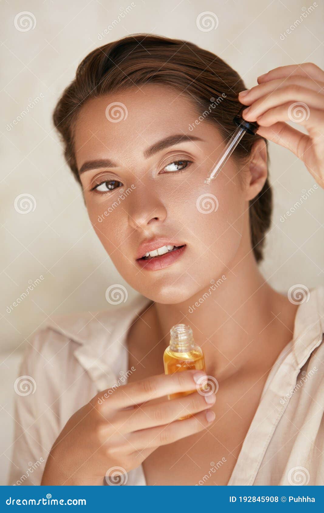 beauty face. woman applying essential oil on facial skin and looking away. beautiful model moisturizing derma.