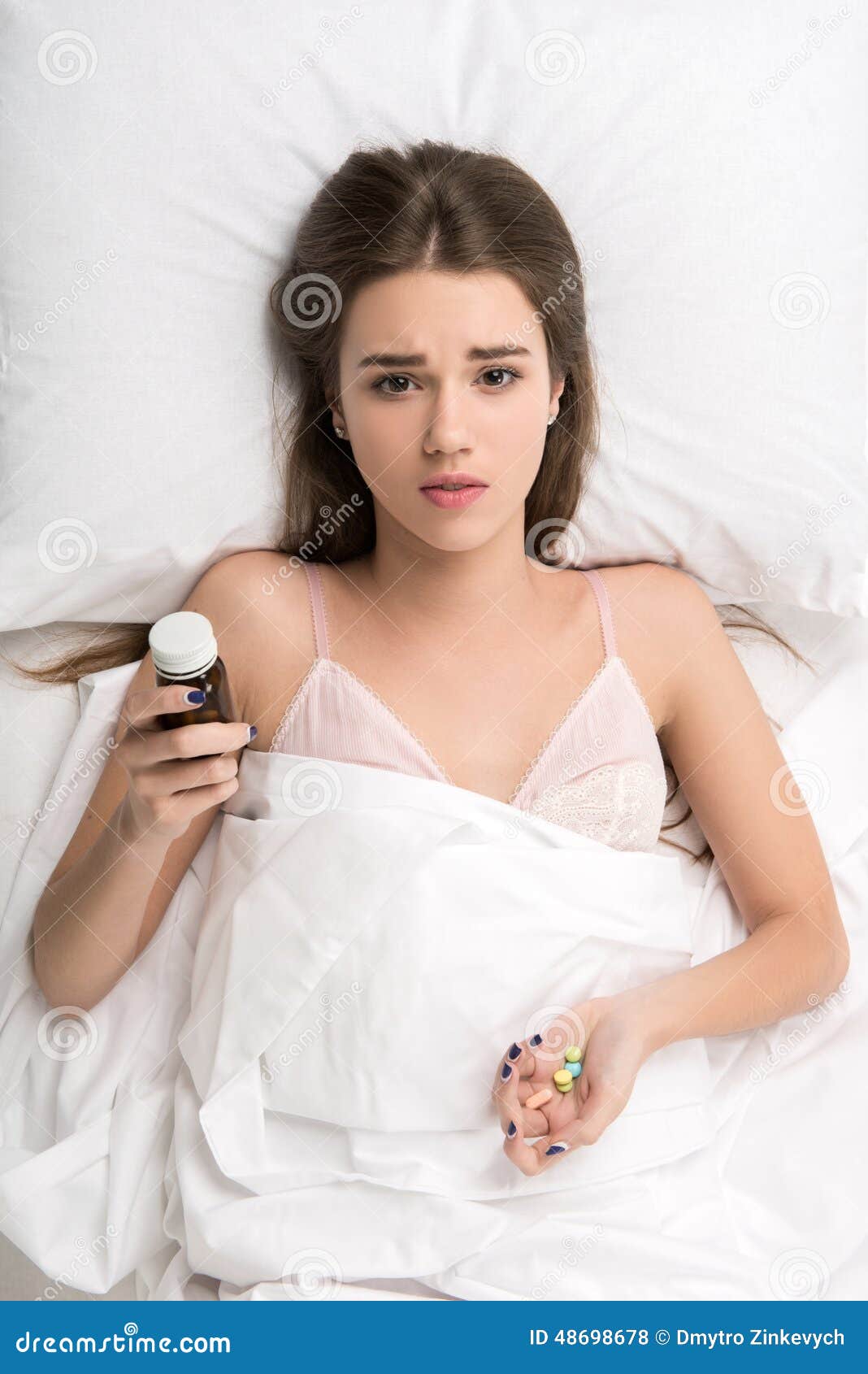 Beauty lying in the bed suffering from insomnia. Sleepless beauty. Beautiful young woman holding bottle and handful of pills while lying on the bed suffering from insomnia