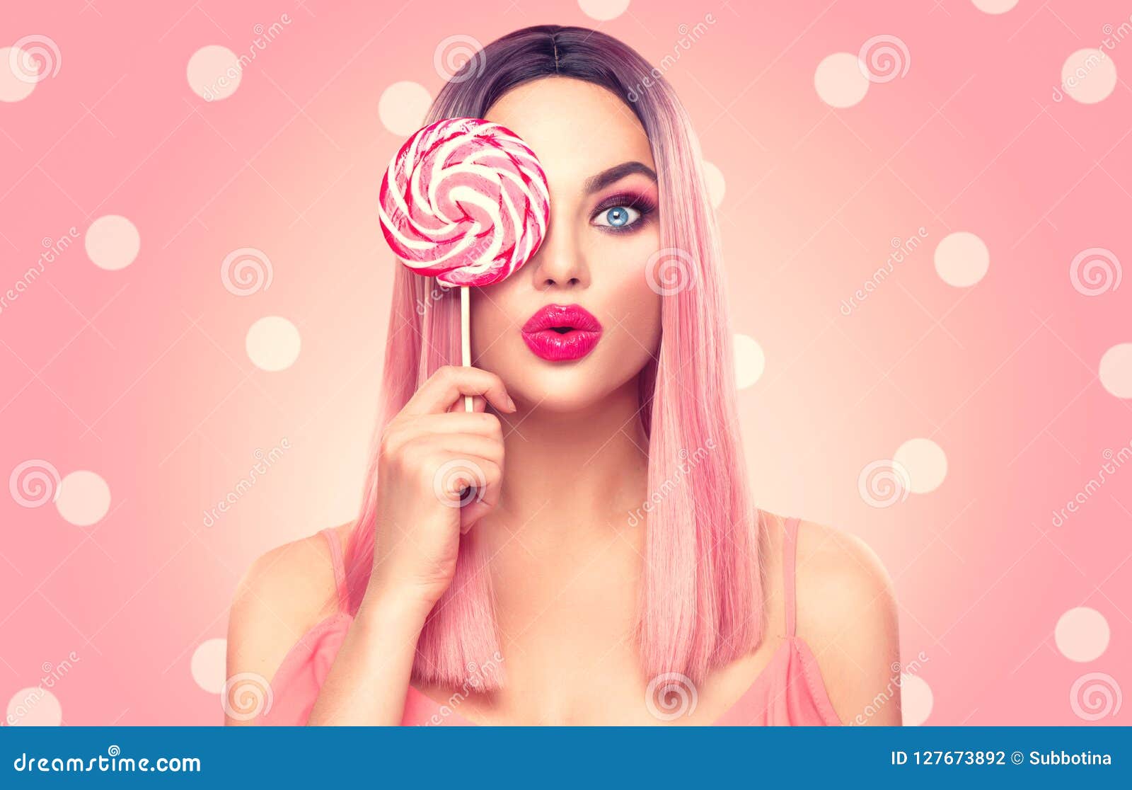 beauty model woman with trendy pink hairstyle and beautiful makeup holding lollipop candy