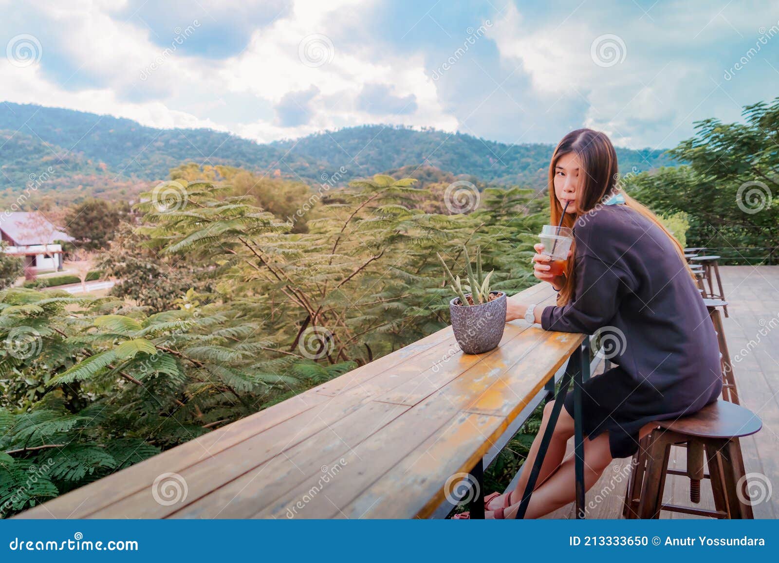 beauty asian smiling female is sitting in cafe with forest and mountain nature background while drinking iced americano