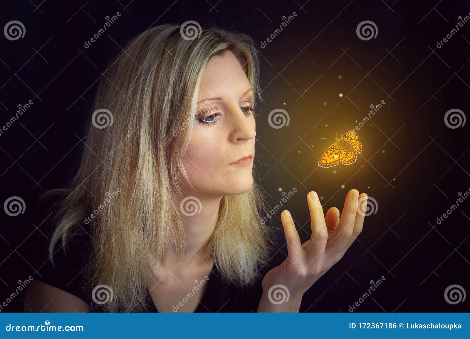 beauty young blond hair woman hold hand under glowing orange butterfly. photomanipulation glowing lepidopteran on black background
