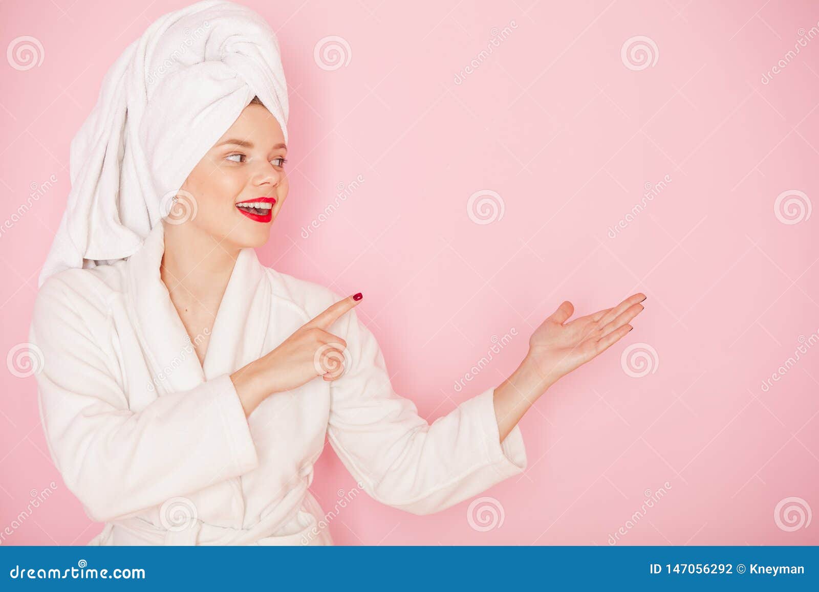 beauty young woman with red lips standing in the bath robe and towel on the head on the pink background. studio shot