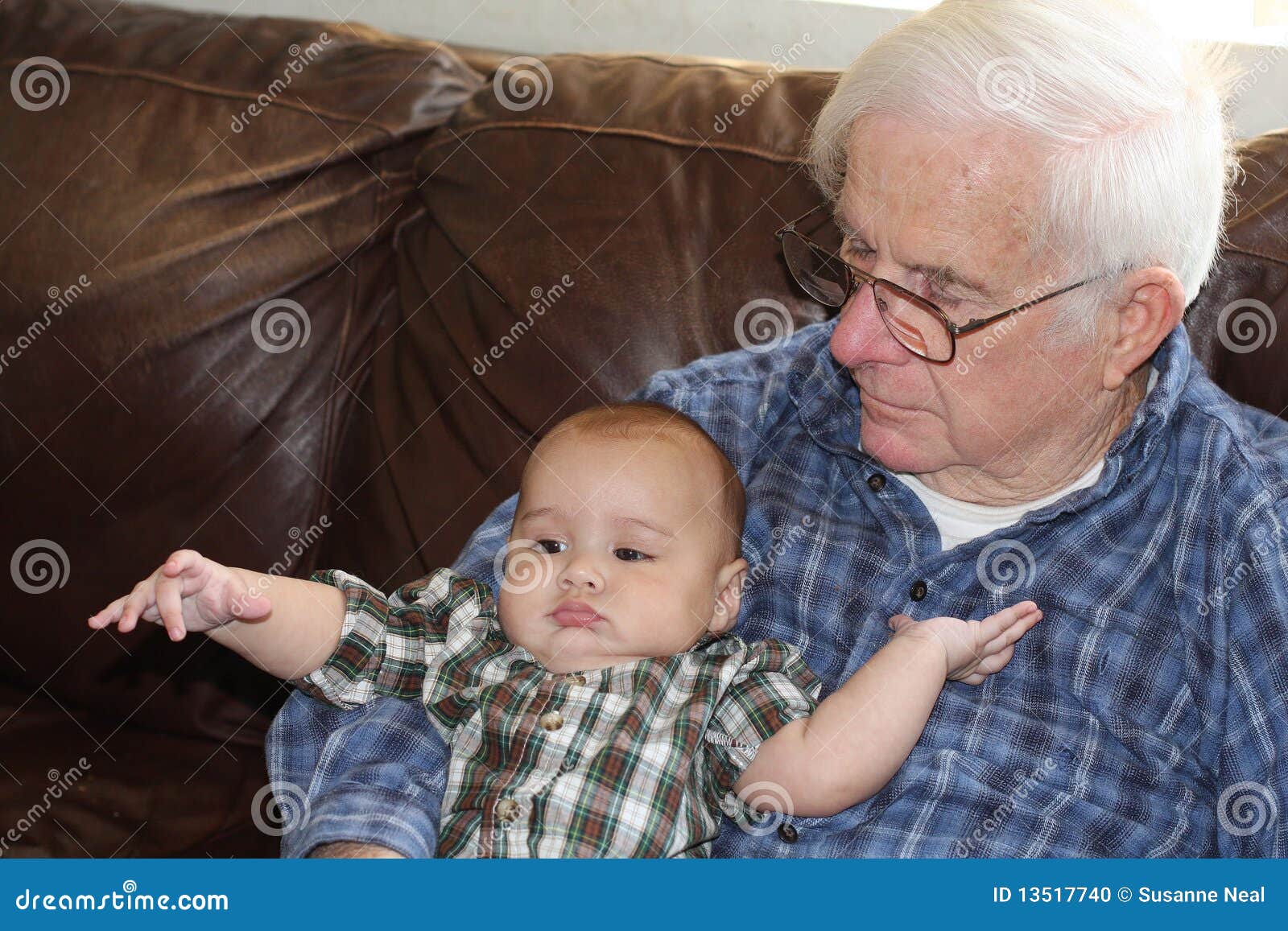 Bebê da terra arrendada do Great-grandpa. Um homem idoso do branco-cabelo prende seu grande - o neto que tem quatro meses velho. Ambos estão desgastando camisas de manta.