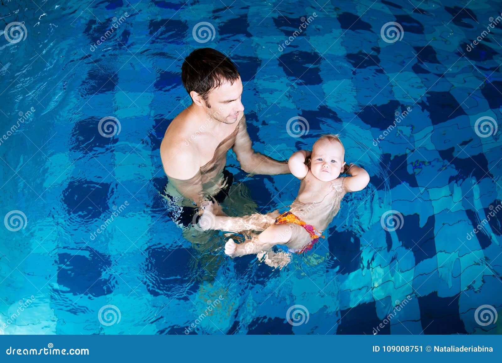 Bebê encantador de sorriso na piscina. Bebê de ensino do pai a nadar Retrato de uns 11 meses de encantamento da criança na sala de aula em uma piscina Vida familiar saudável