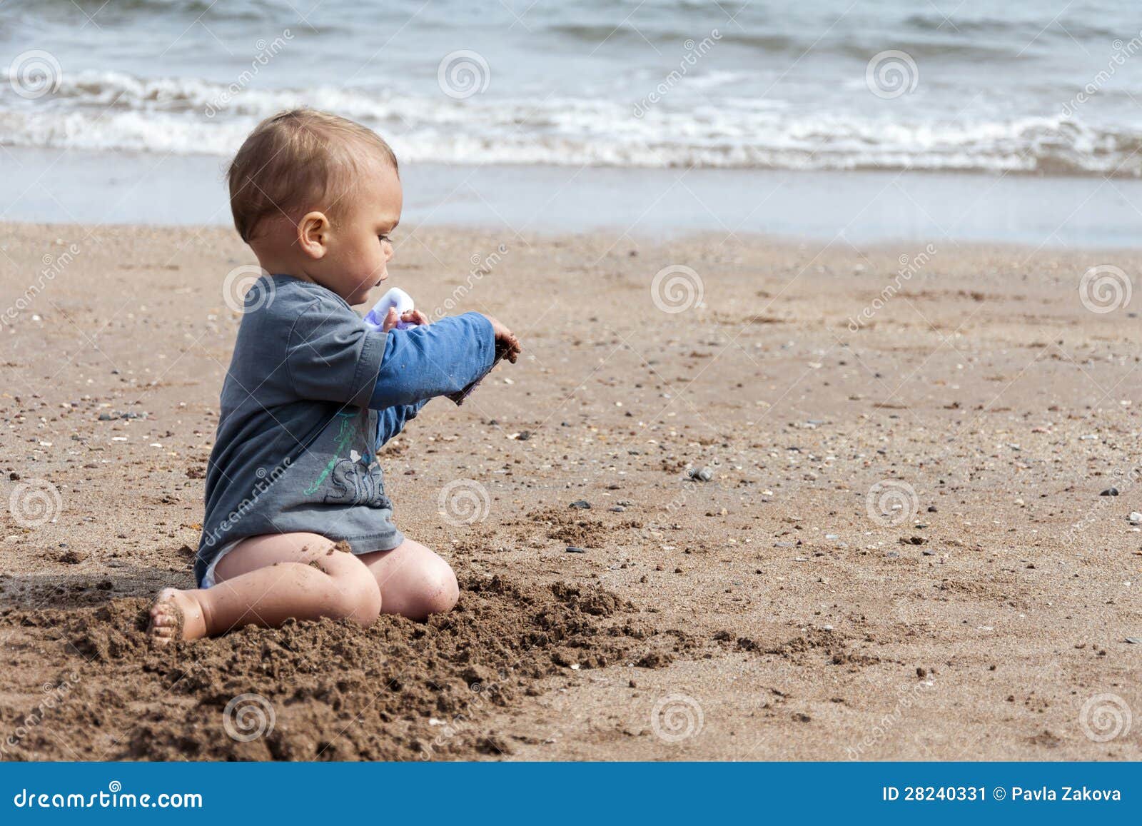 Bebê na praia. Bebê ou uma criança da criança, um menino ou uma menina pequena, jogando com uma areia em uma praia.