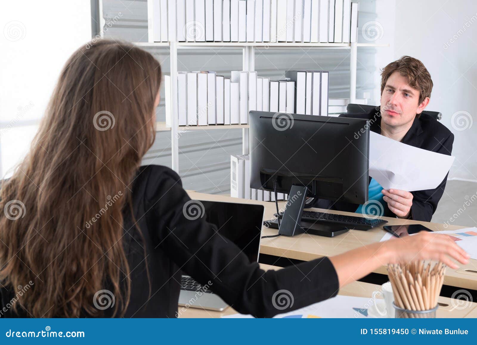 Bedrijfscollega's vergadering in het huisbureau hebben, of twee jonge medewerkers die aan laptop computer op modern kantoor werke. De bedrijfscollega's vergadering in het huisbureau hebben, of twee jonge medewerkers die aan laptop computer op modern kantoor, het document van de zakenmanholding document werken en vragen het statuut van het project