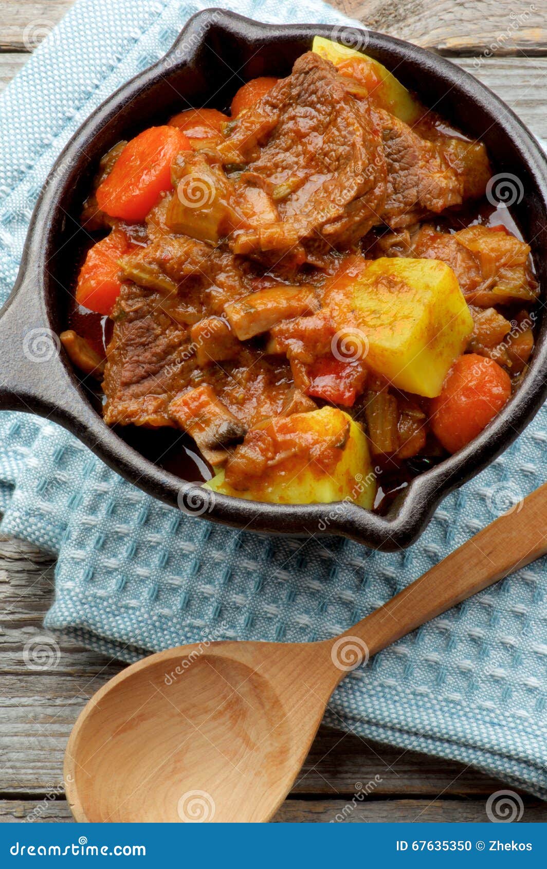 Beef and Vegetables Stew. Delicious Beef Stew with Carrots, Potatoes, Celery and Leek in Cast Iron on Blue Napkin with Wooden Spoon closeup. Top View