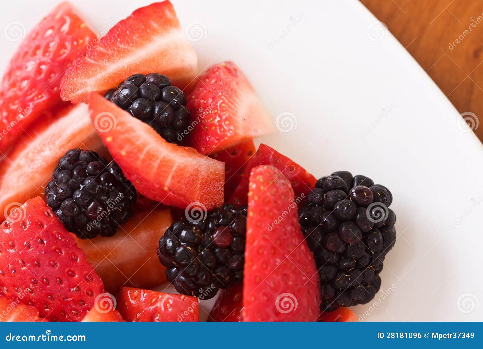 Nahaufnahme von geschnittenen frischen Erdbeeren mit Brombeeren auf einer weißen Platte