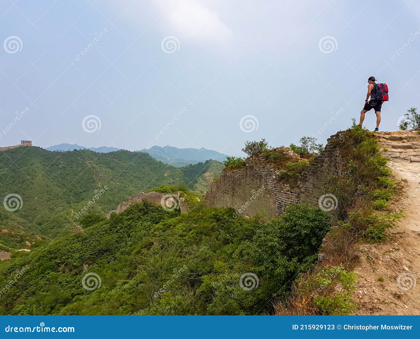 beijing - a man with hiking backpack walking around a unrenewed gubeikou part of great wall of china. the wall is spreading