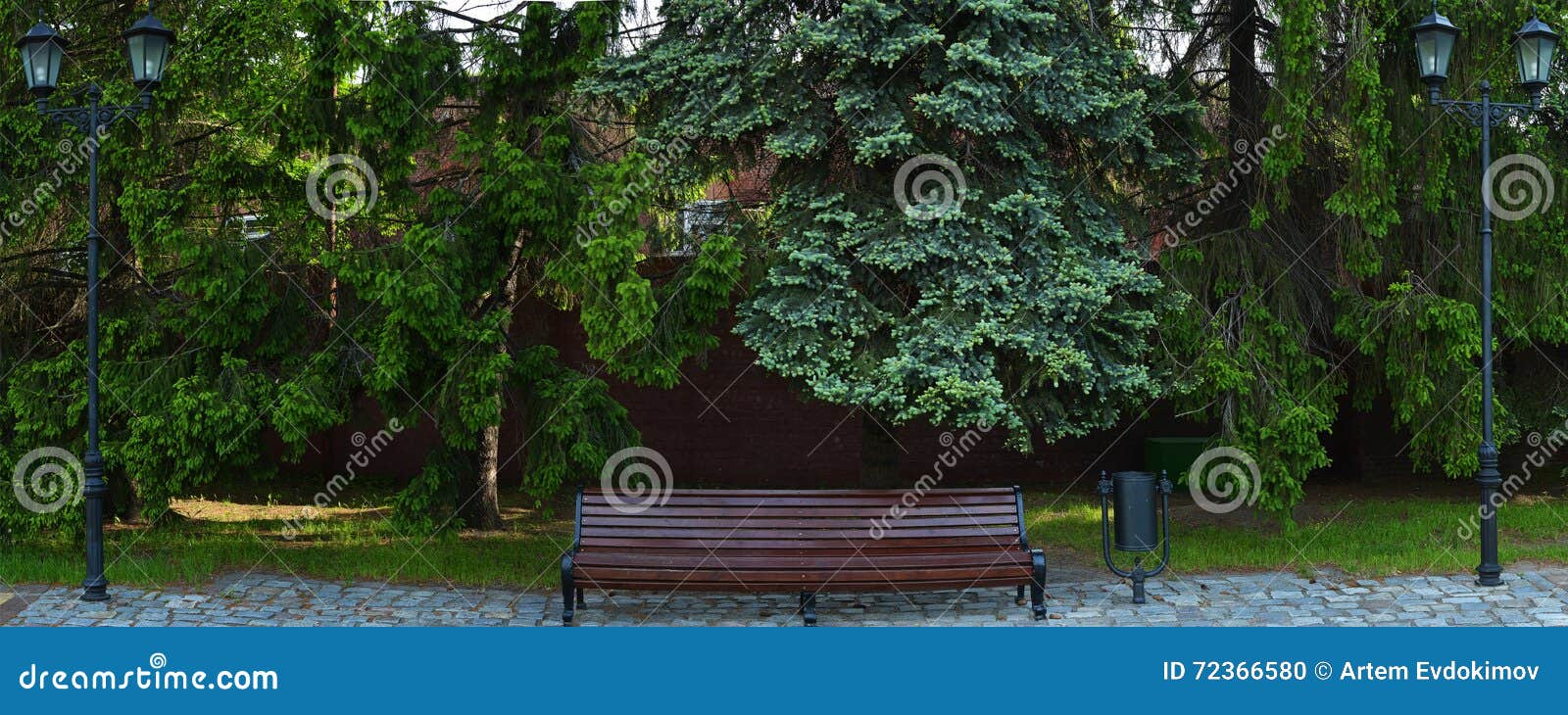 Bench in primavera il parco con due lampade di via, i pini ed il Br rosso. Parco del banco di legno in primavera con due pali della luce, i pini ed il fondo rosso del muro di mattoni Panorama