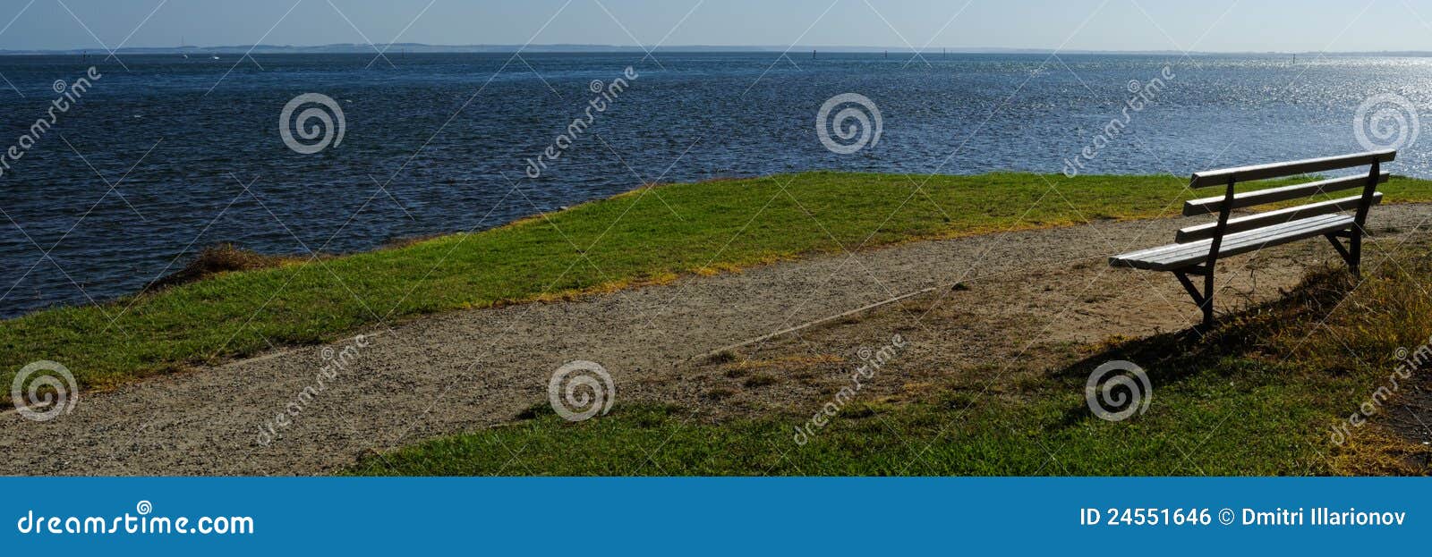 Bench at Western Port. Panorama of with wooden bench at calm blue seas of Western Port, bright sunlight, glare on water with light wind, on green grass in Victoria, Australia