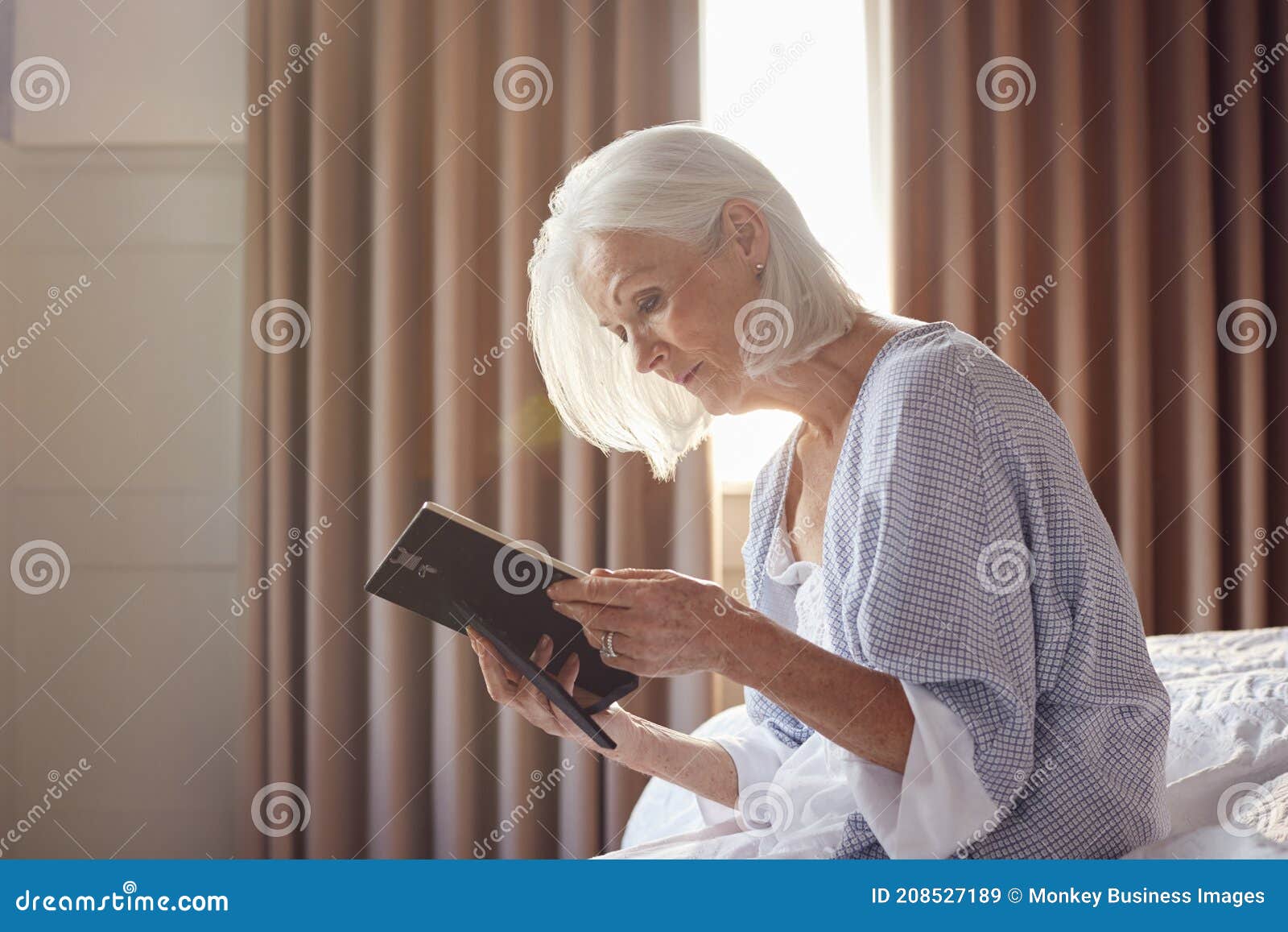 bereaved senior woman sitting on edge of bed looking at photo in frame