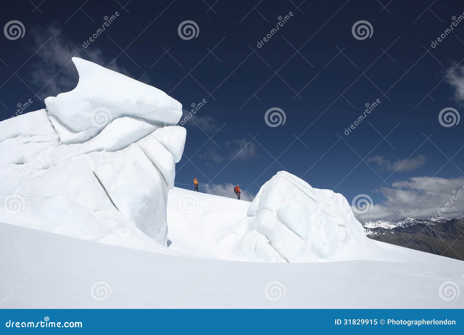 Bergsbestigare som går förbi isbildande. Sidosikt av två fotvandrare som går förbi isbildande på ett avstånd i snöig berg